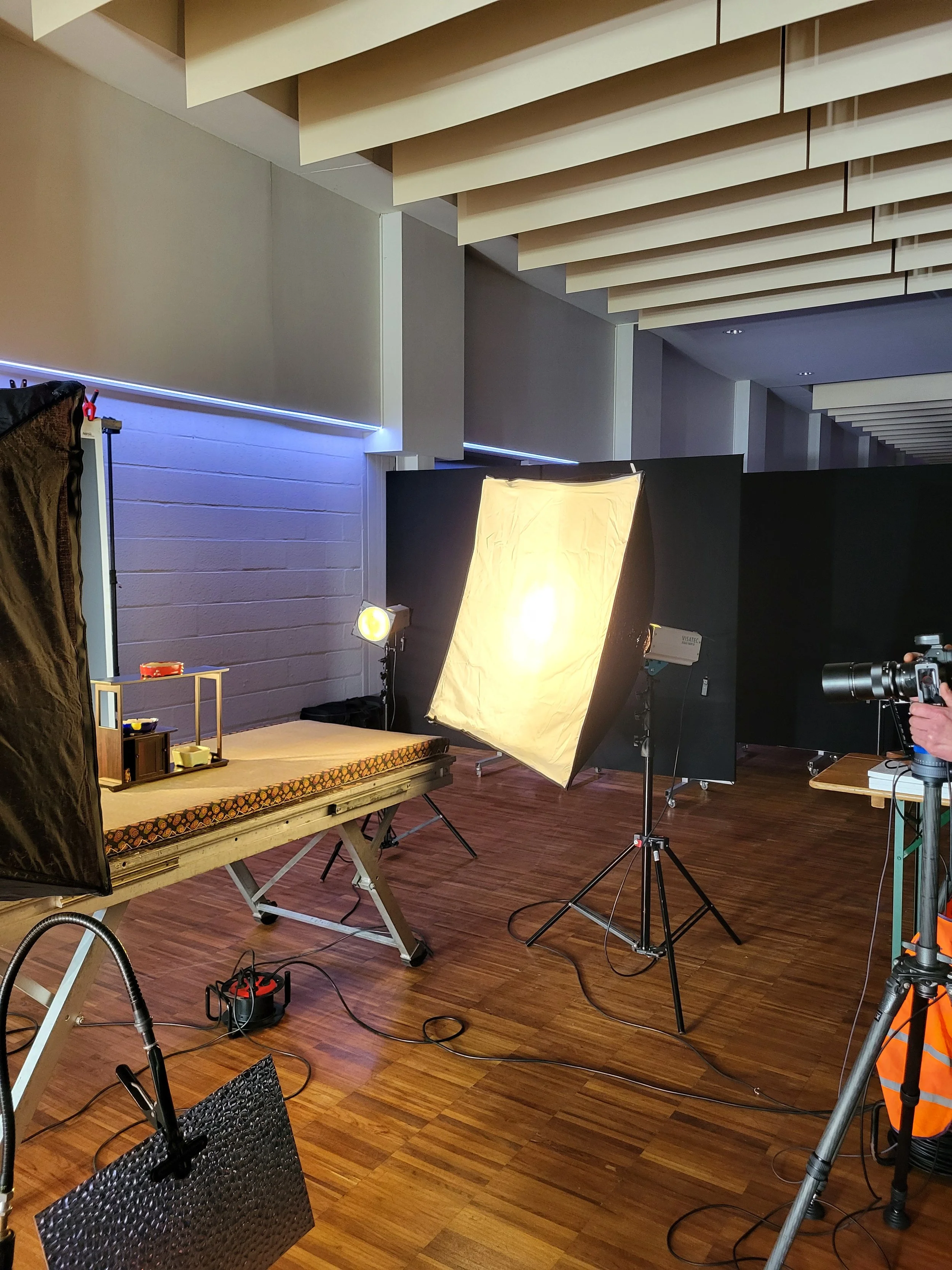 Photography studio with lighting equipment, a backdrop, and a model's bed setup for a photo shoot.