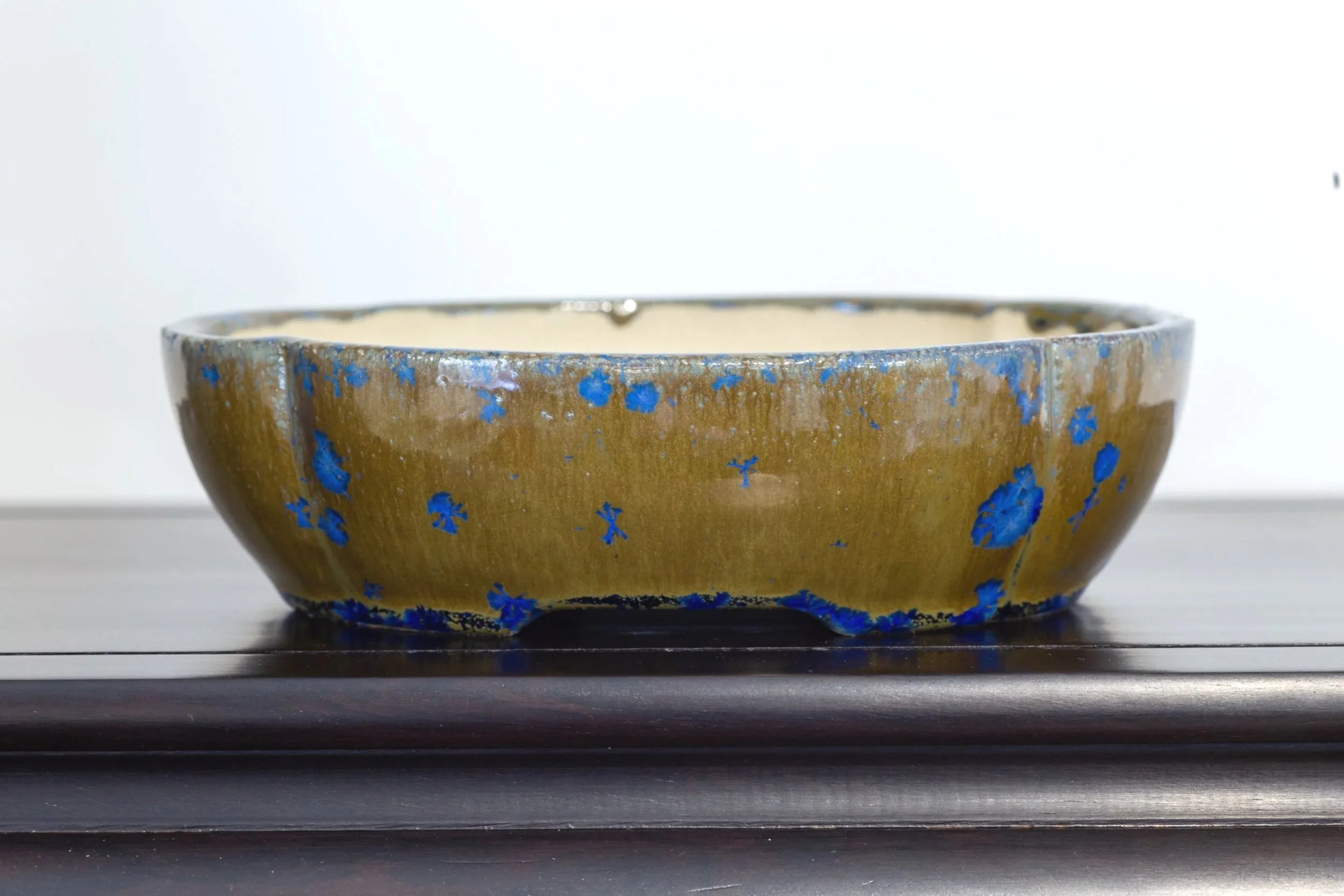 A ceramic bowl with blue floral patterns on an earthy brown background, empty, placed on a wooden surface against a plain white backdrop.