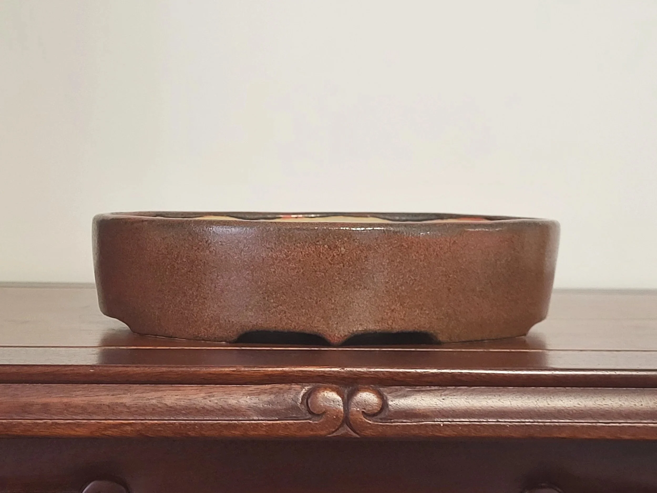 A brown ceramic bowl with a textured surface sits on a wooden surface against a plain background.