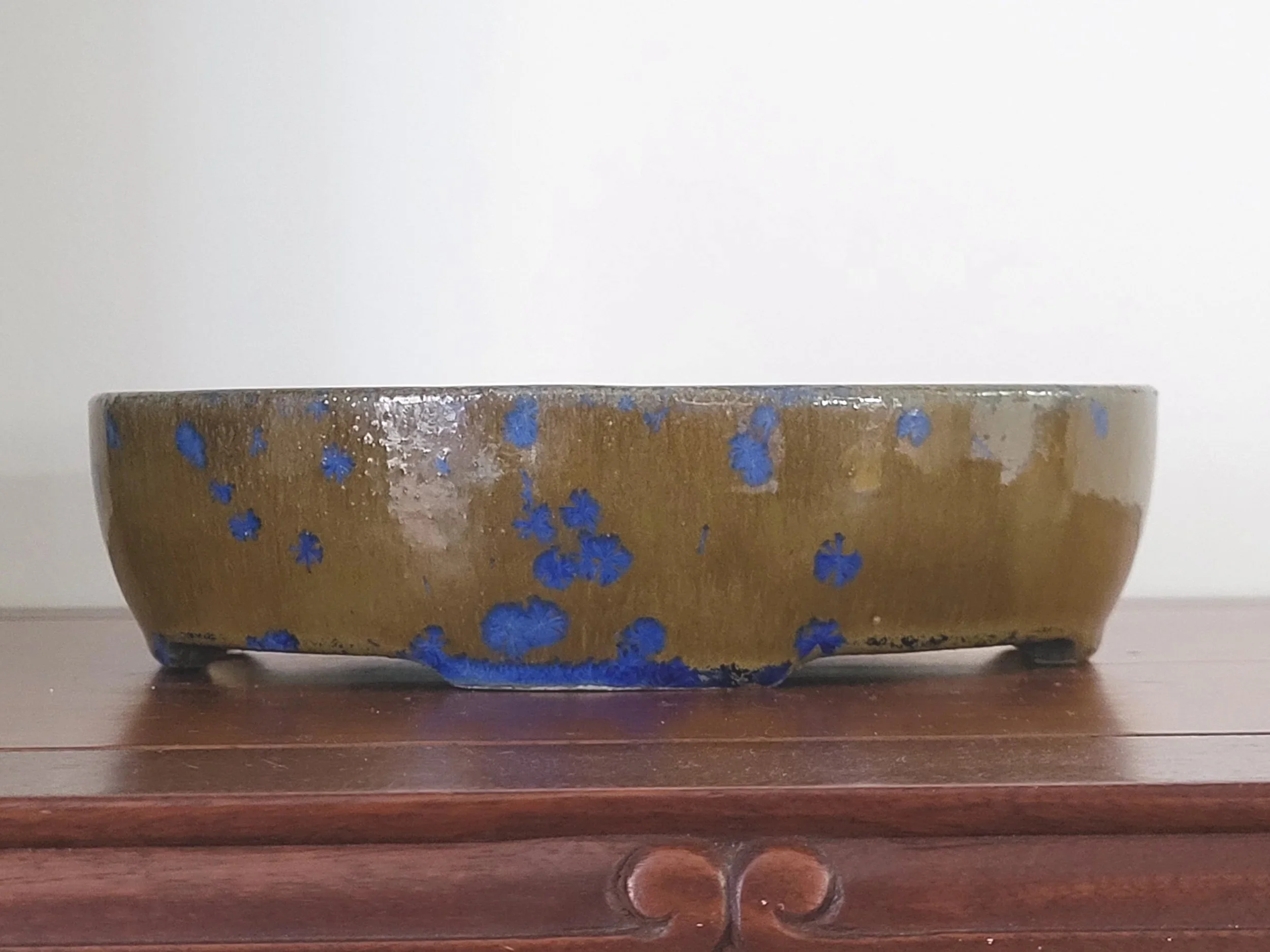 A shallow round ceramic bowl with a brown glaze and blue floral patterns, sitting on a wooden surface.