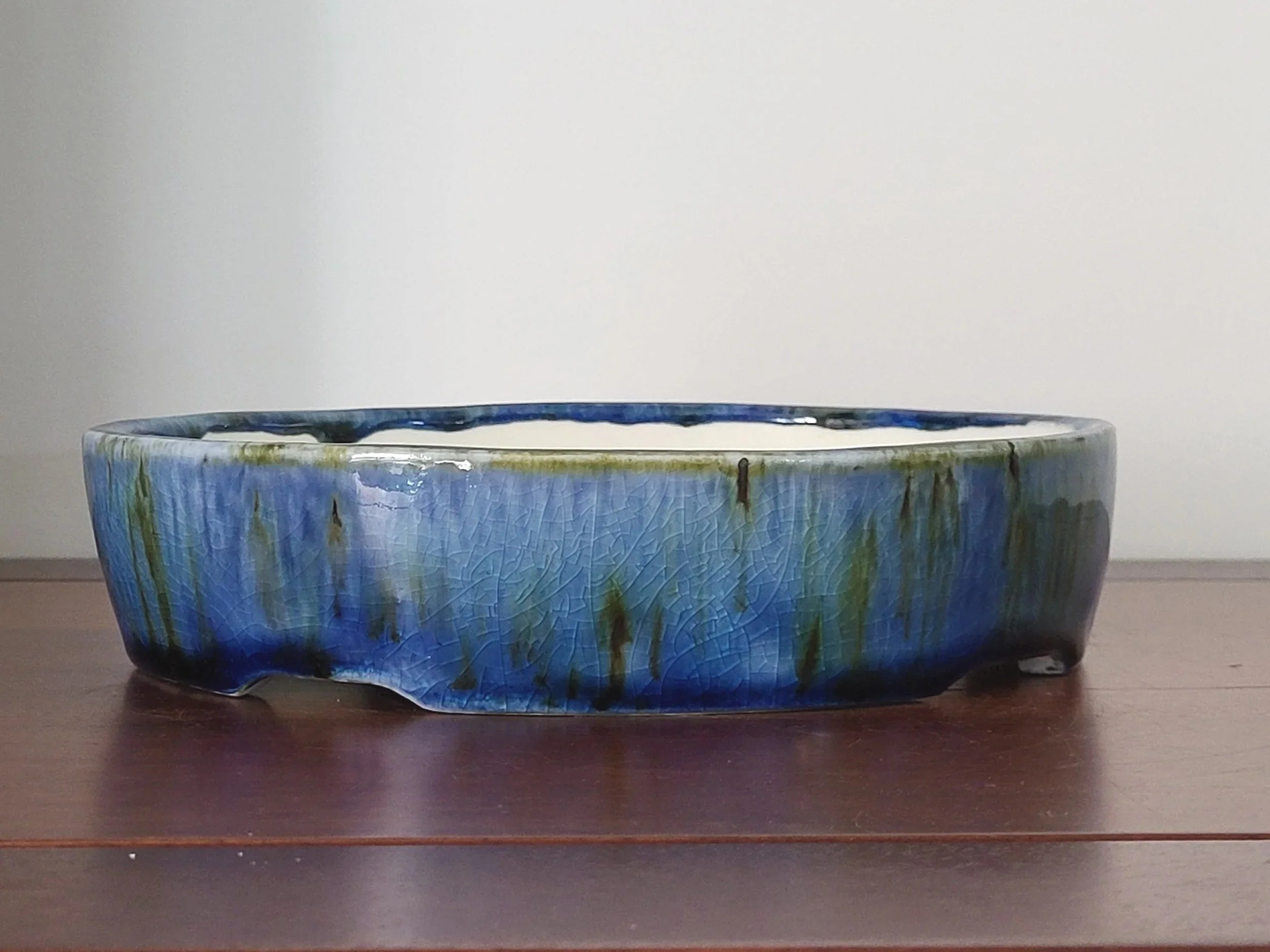 A pottery bowl with a crackle glaze in shades of blue, green, and black, sitting on a wooden surface against a plain wall.