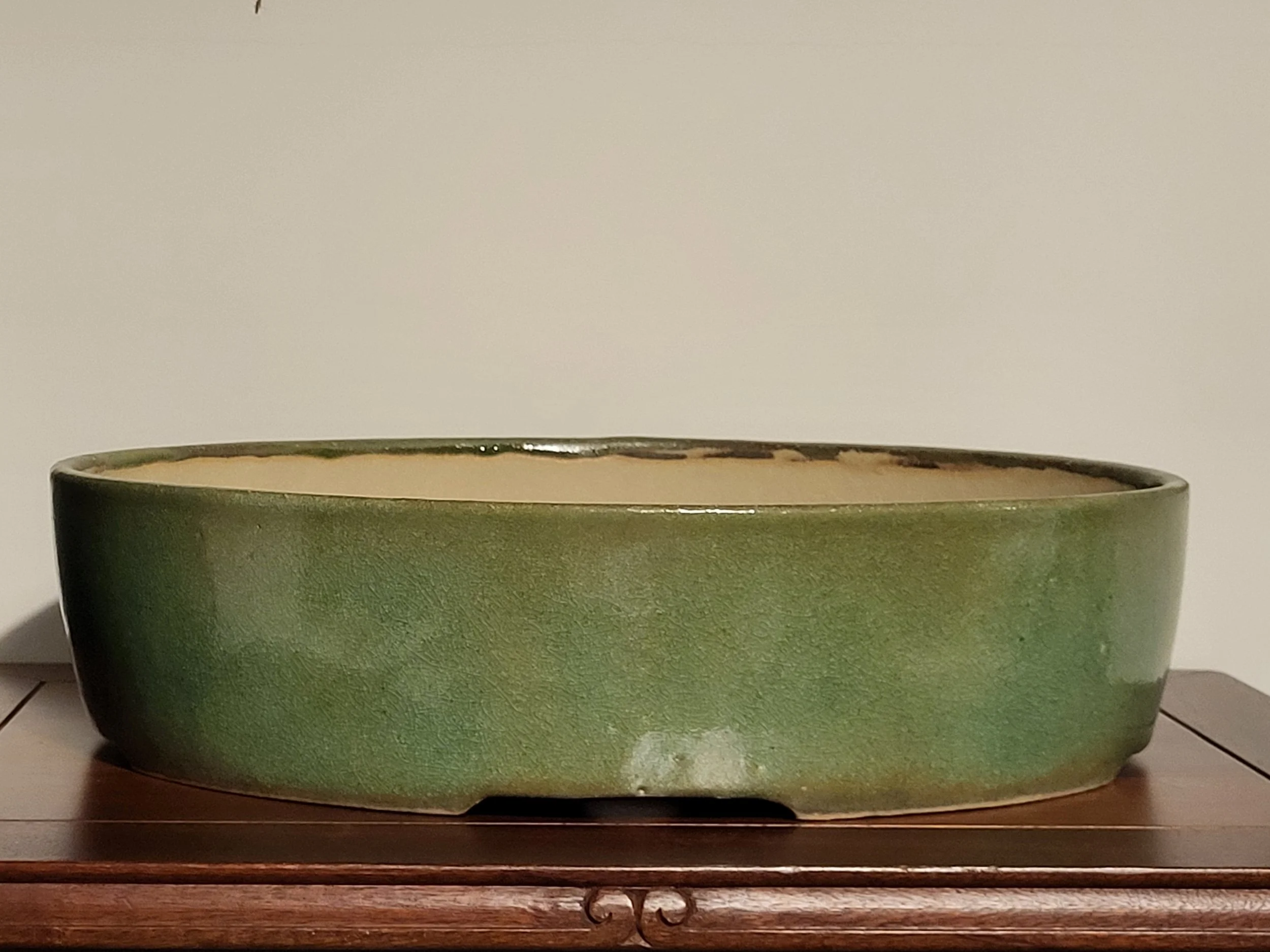 A large round green ceramic bowl placed on a wooden table against a plain background.