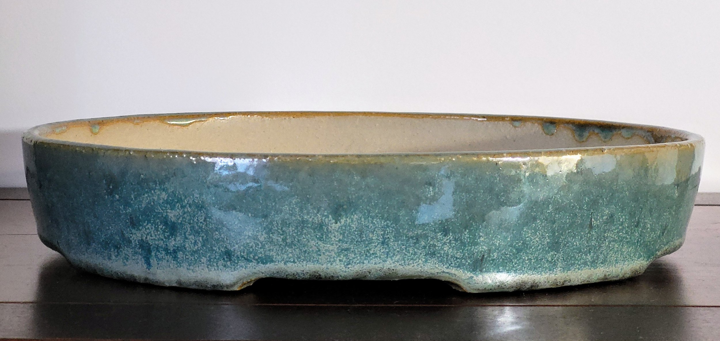 A large ceramic bowl with a mottled blue-green glaze and a beige interior, placed on a dark wooden surface.