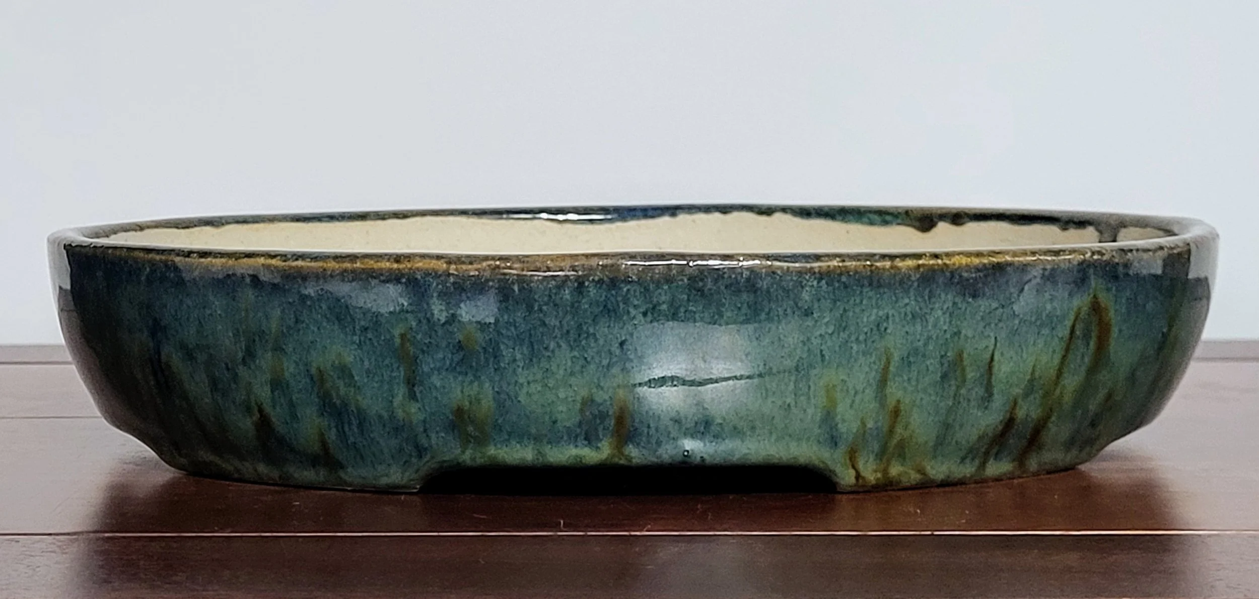 A large ceramic bowl with a green glaze and brown accents on a wooden surface.