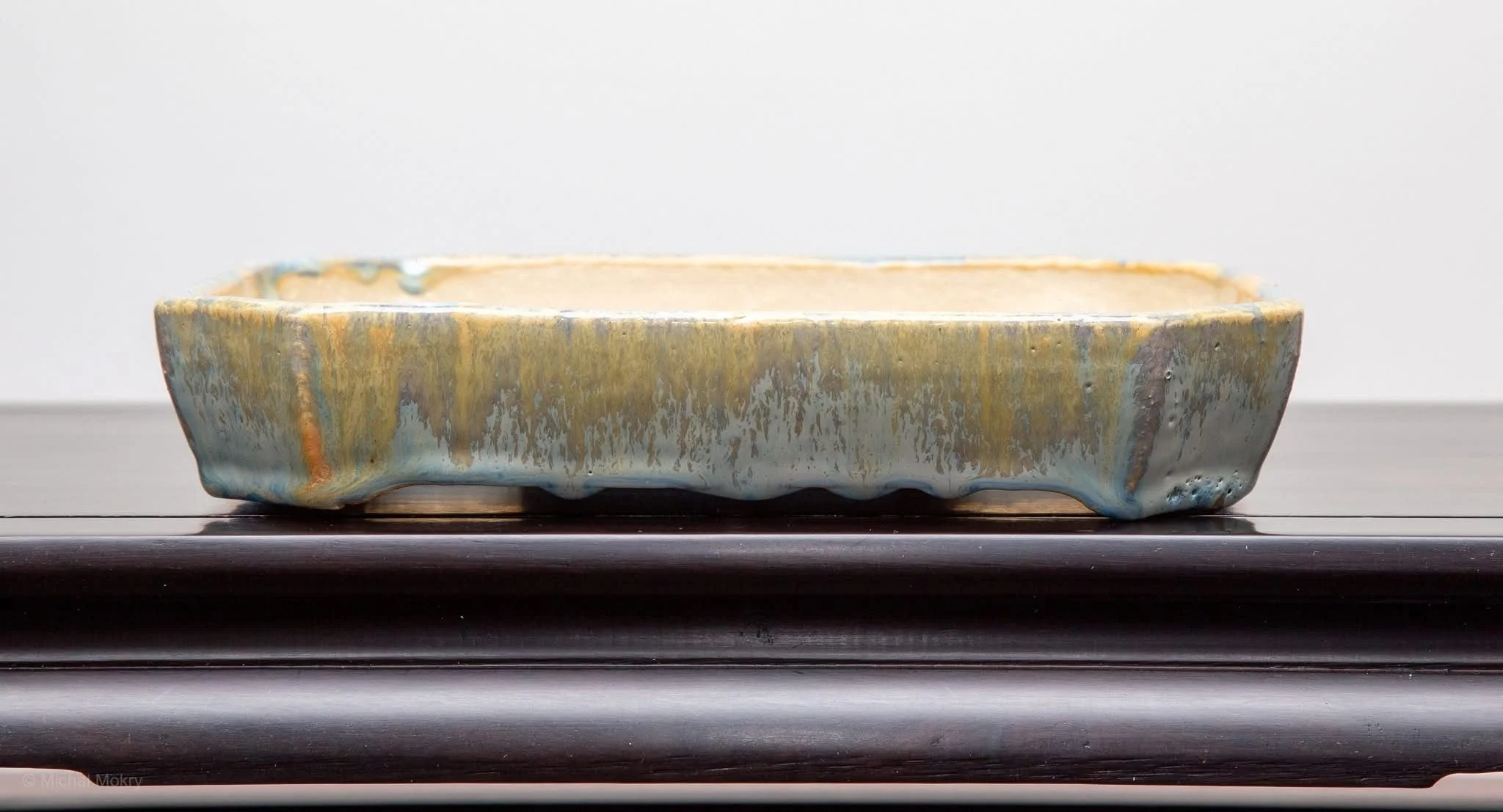 A rectangular ceramic dish with a glaze that has blue, green, and orange streaks, resting on a dark wooden surface.