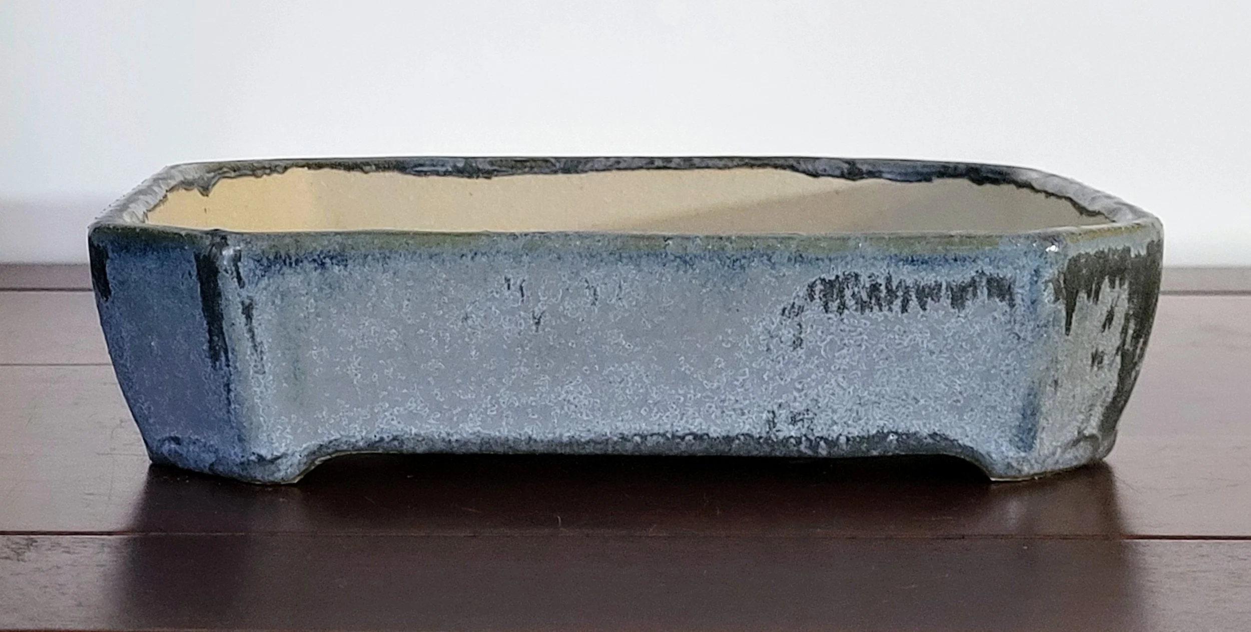 A rectangular, weathered bonsai tree pot with a rough surface on a dark wooden table.