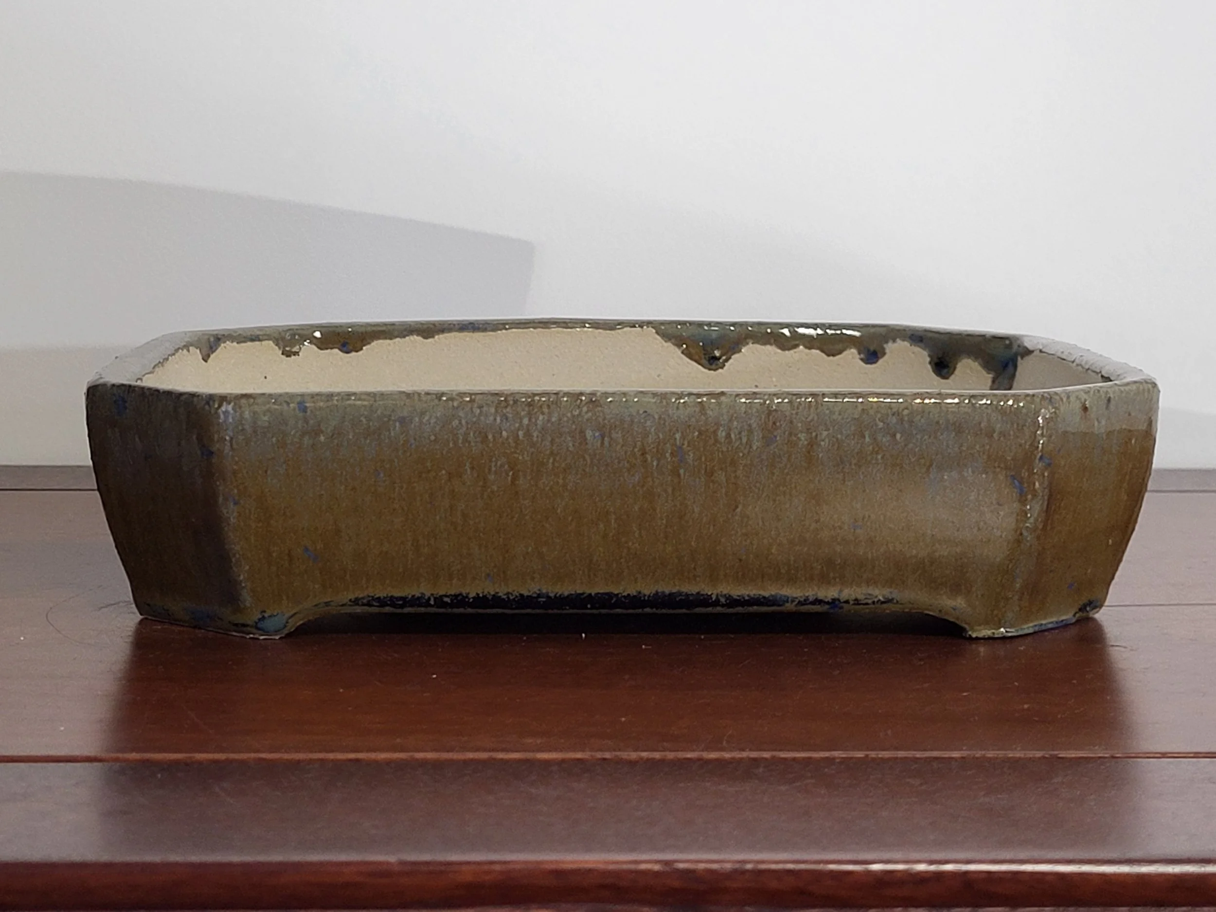 Rectangular ceramic planter with a glazed dark brown exterior and an unglazed beige interior, sitting on a wooden surface.