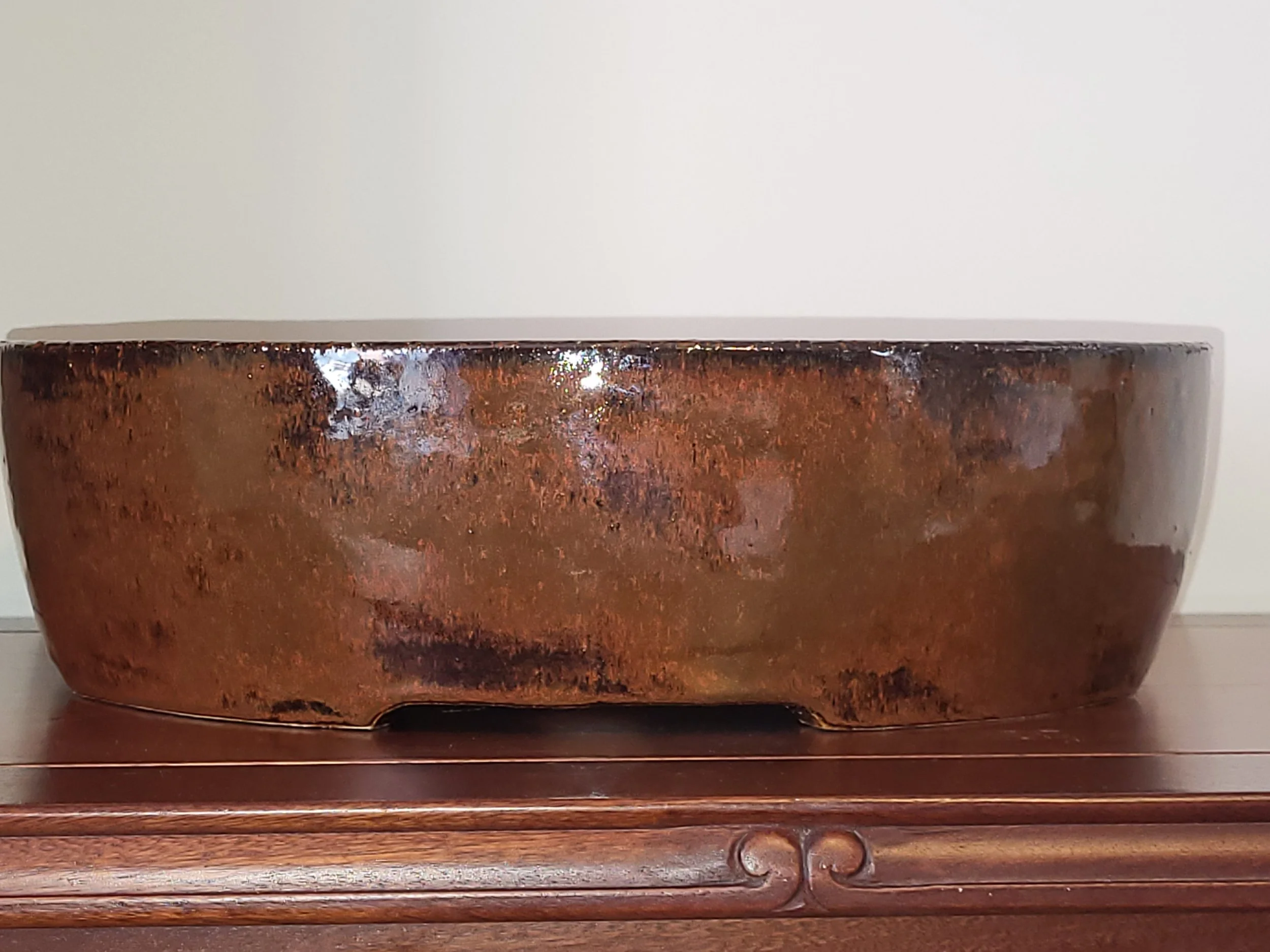 Close-up of a large, round, rust-colored ceramic bowl with a glossy finish resting on a wooden surface.
