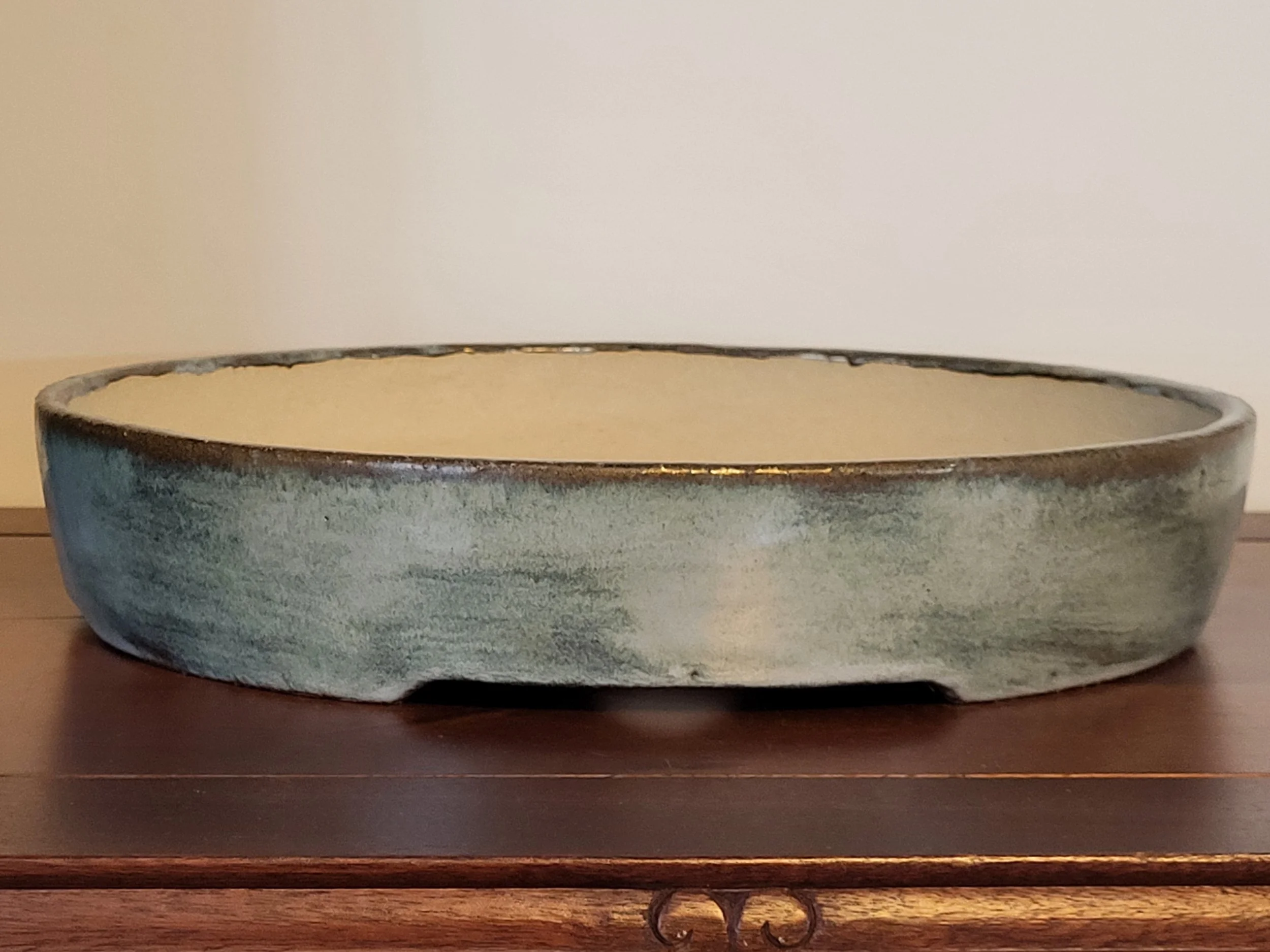 A shallow ceramic bowl with a glazed outer surface featuring shades of green and gray, sitting on a wooden surface against a plain background.