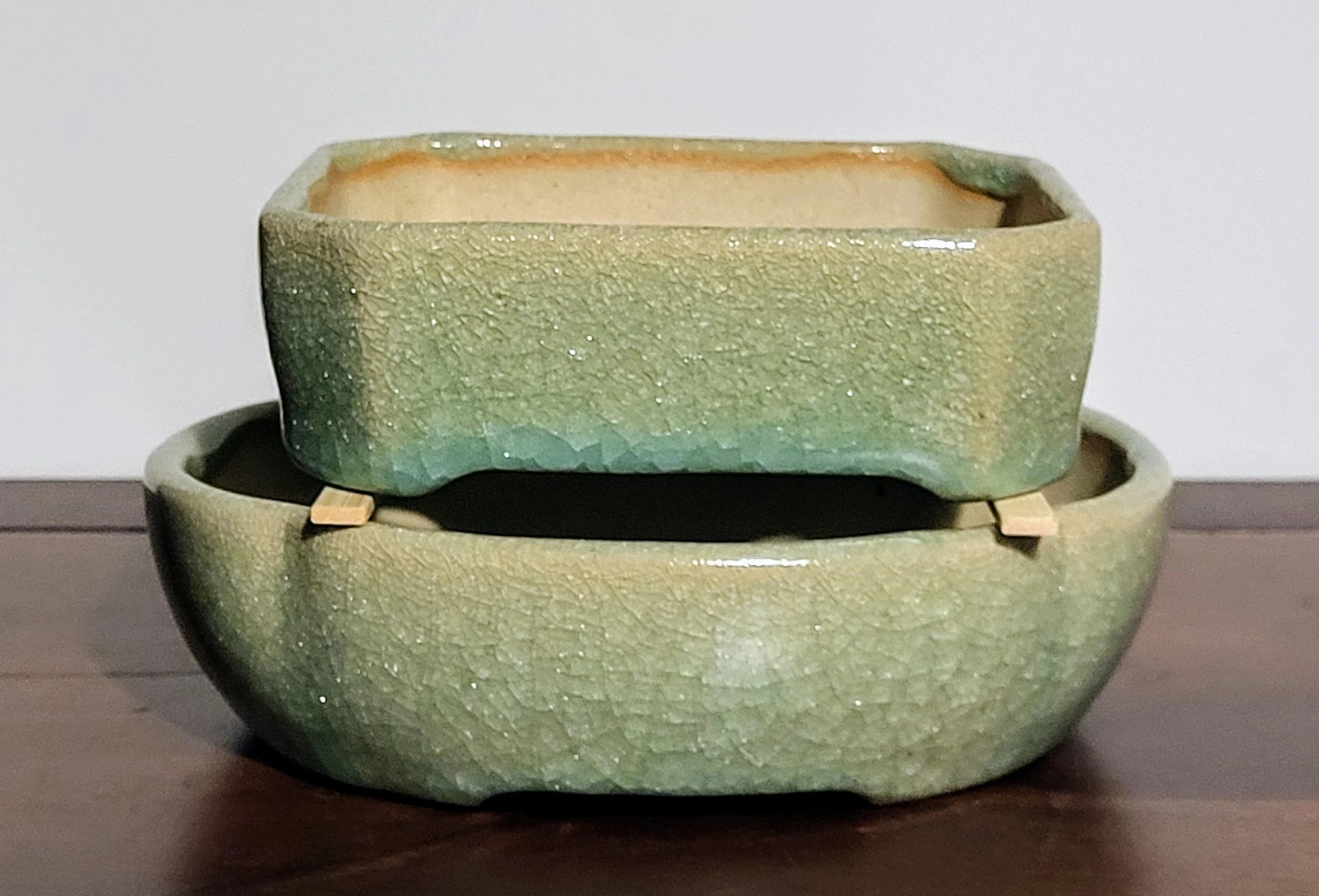 Two stacked glazed ceramic bowls with a crackled green glaze on a wooden surface.