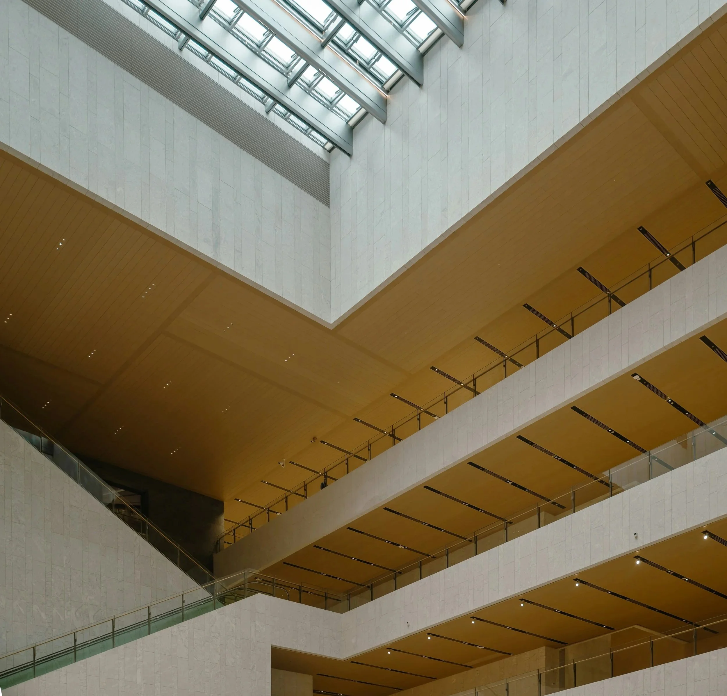 Interior of a modern multi-story building with open levels, a large skylight, and wooden ceiling panels.