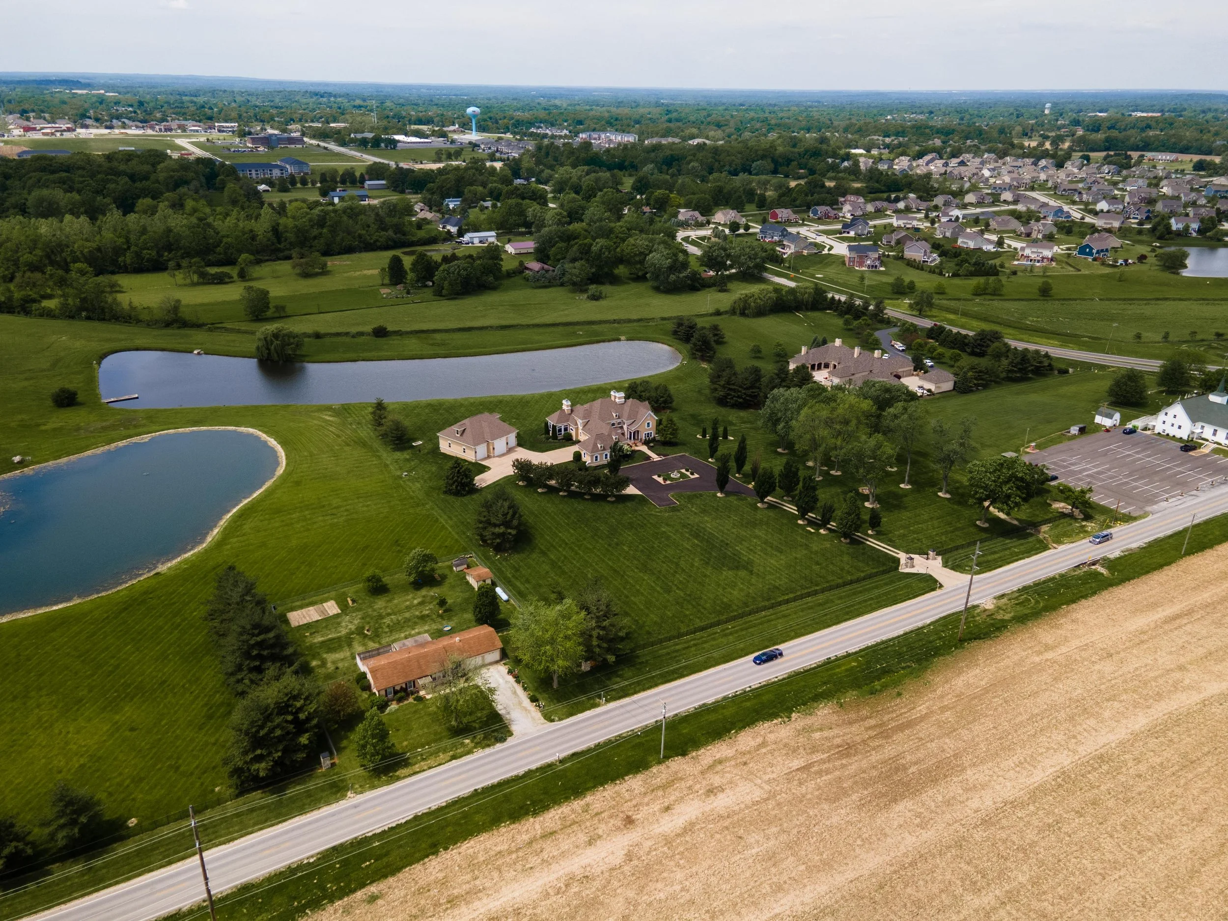 Aerial view of a suburban area with houses, lakes, trees, and a road in the foreground.