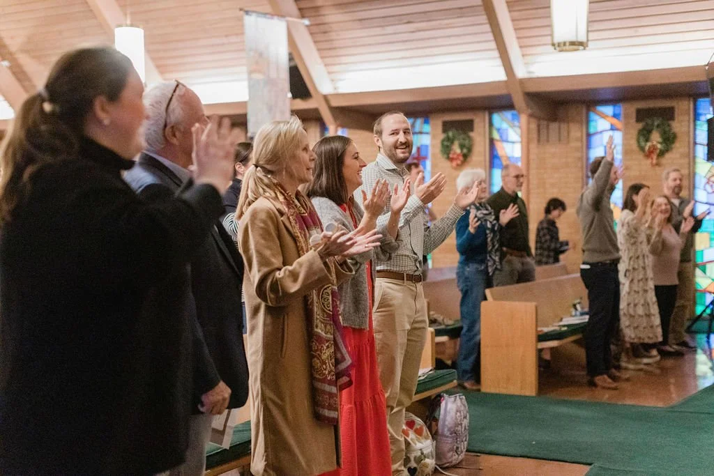 People standing in a church, clapping and smiling during a service or celebration.