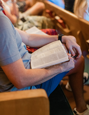 Person sitting in church pew holding an open book, likely a Bible.