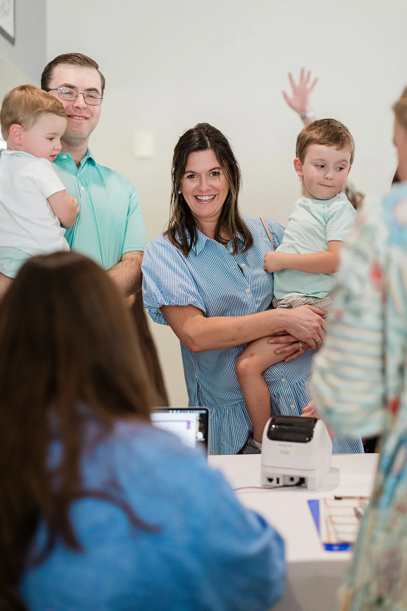 A smiling woman holding a young boy, with a man and another child standing nearby, at a crowded indoor event.