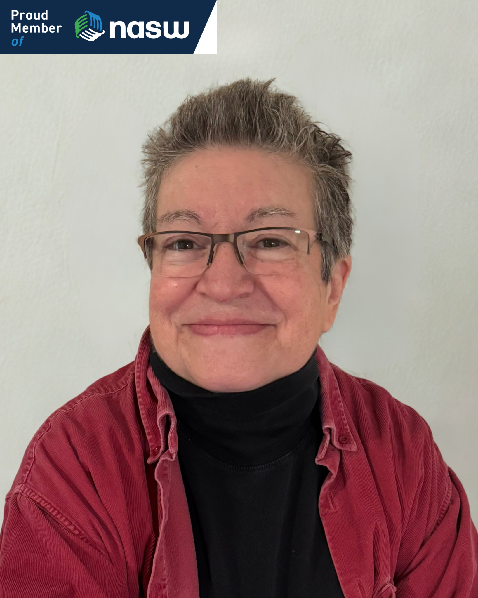 Smiling person with glasses, wearing a red shirt over a black turtleneck, against a white wall. NASW logo in the top left corner.
