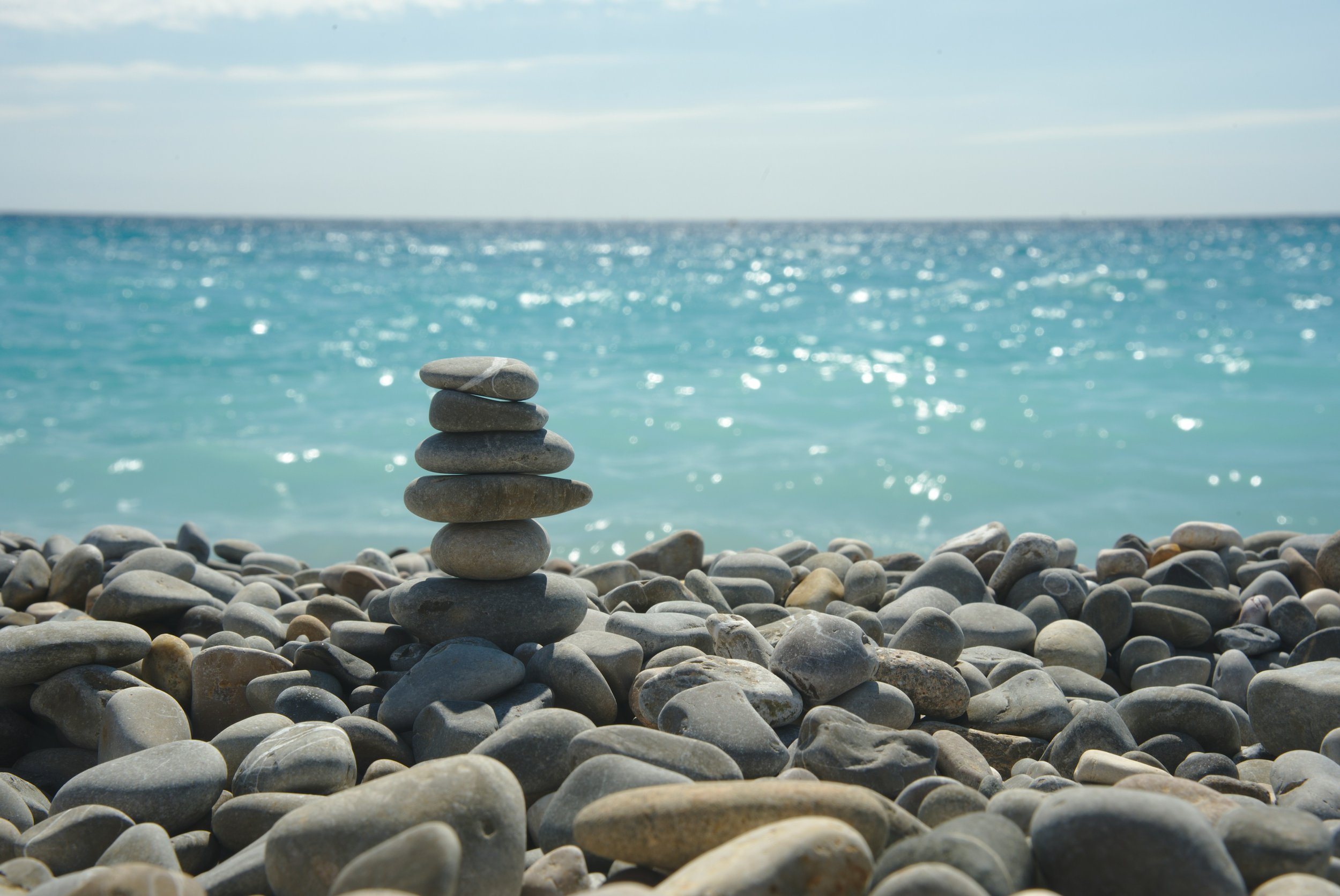 Stacked smooth stones on a pebble beach with the ocean and sky in the background.