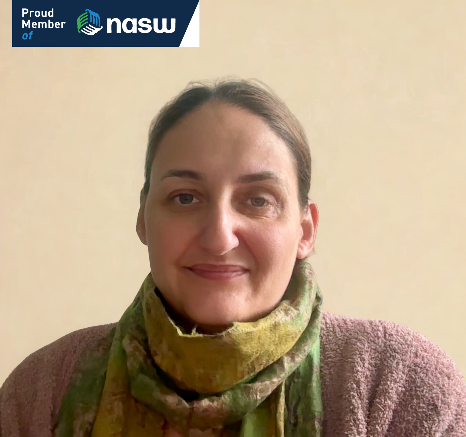 A woman with light skin and brown hair pulled back, wearing a multicolored scarf and a pinkish-brown sweater, smiling in front of a plain beige wall. A NASW logo is in the top left corner.