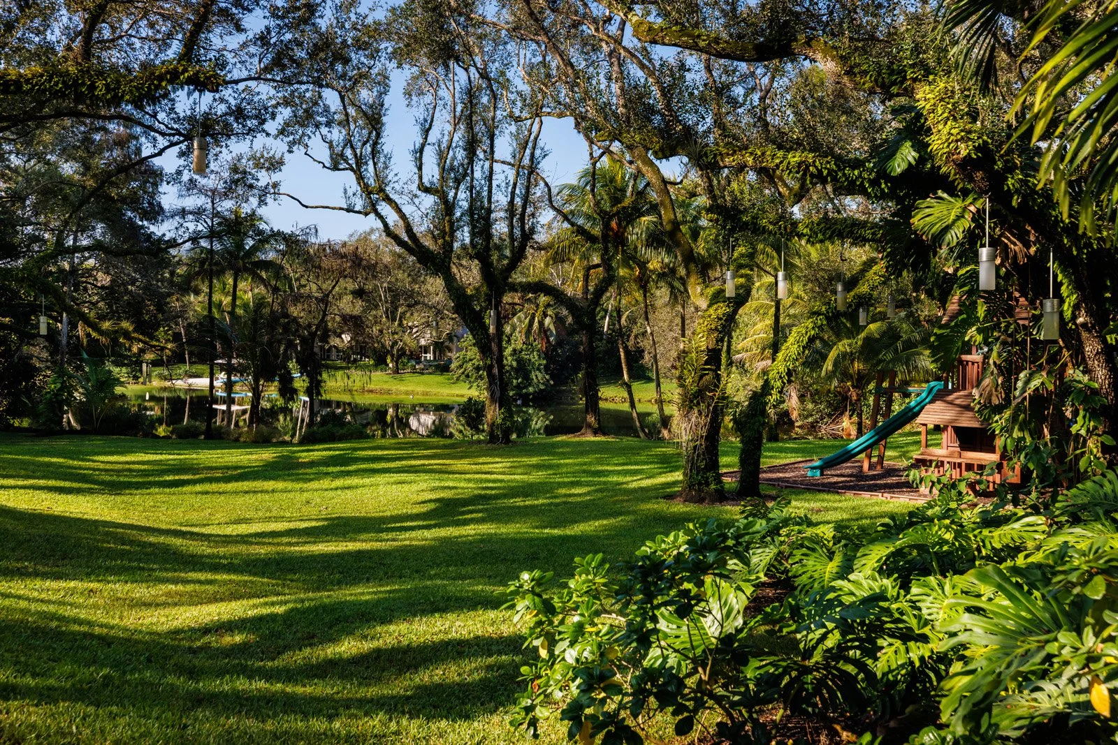 A landscaped backyard with a grassy lawn, trees, a pond, and a children's play area with a slide.
