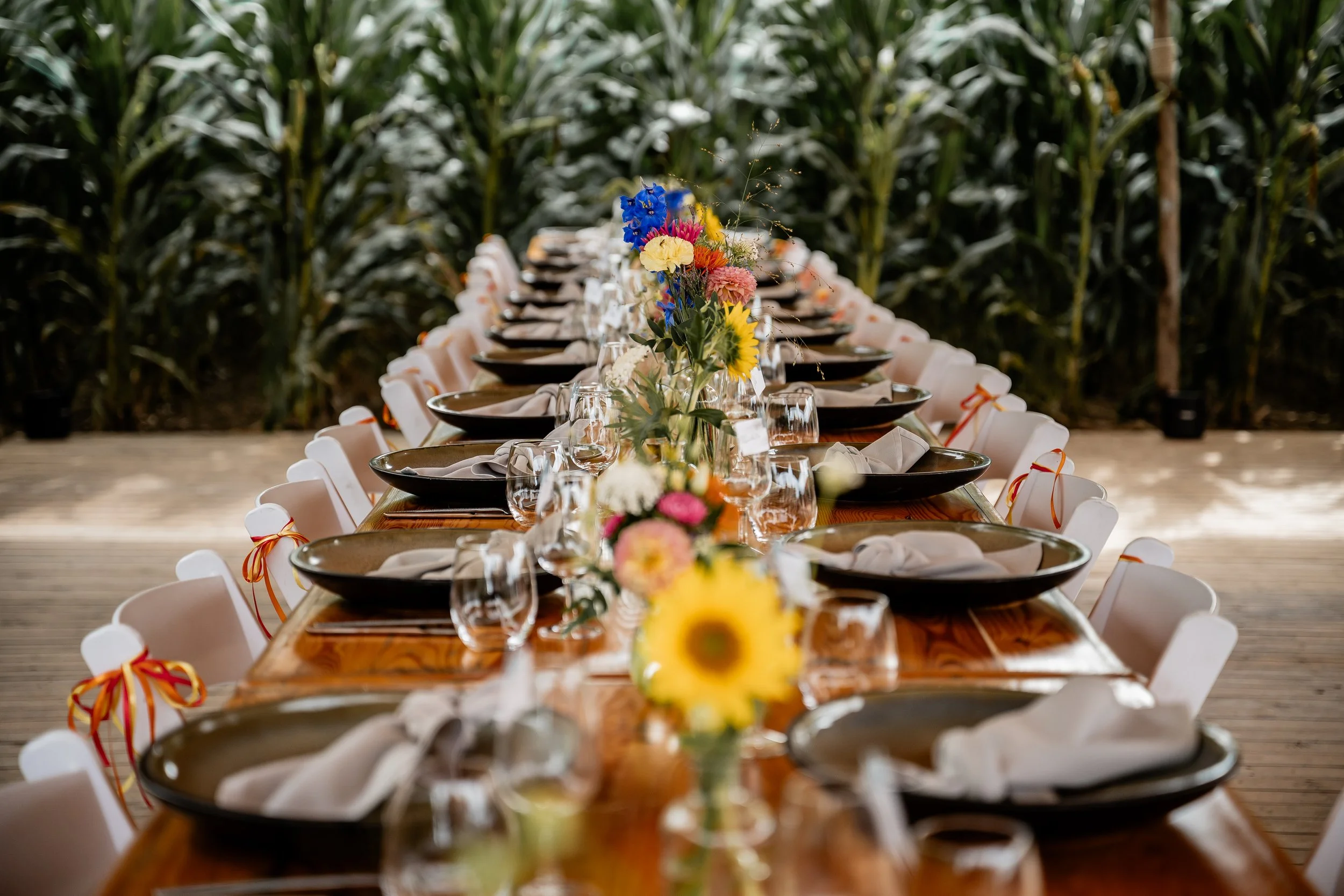 Lange met borden gedekte tafel en bloemen in een natuurlijke setting voor een bruiloft.
