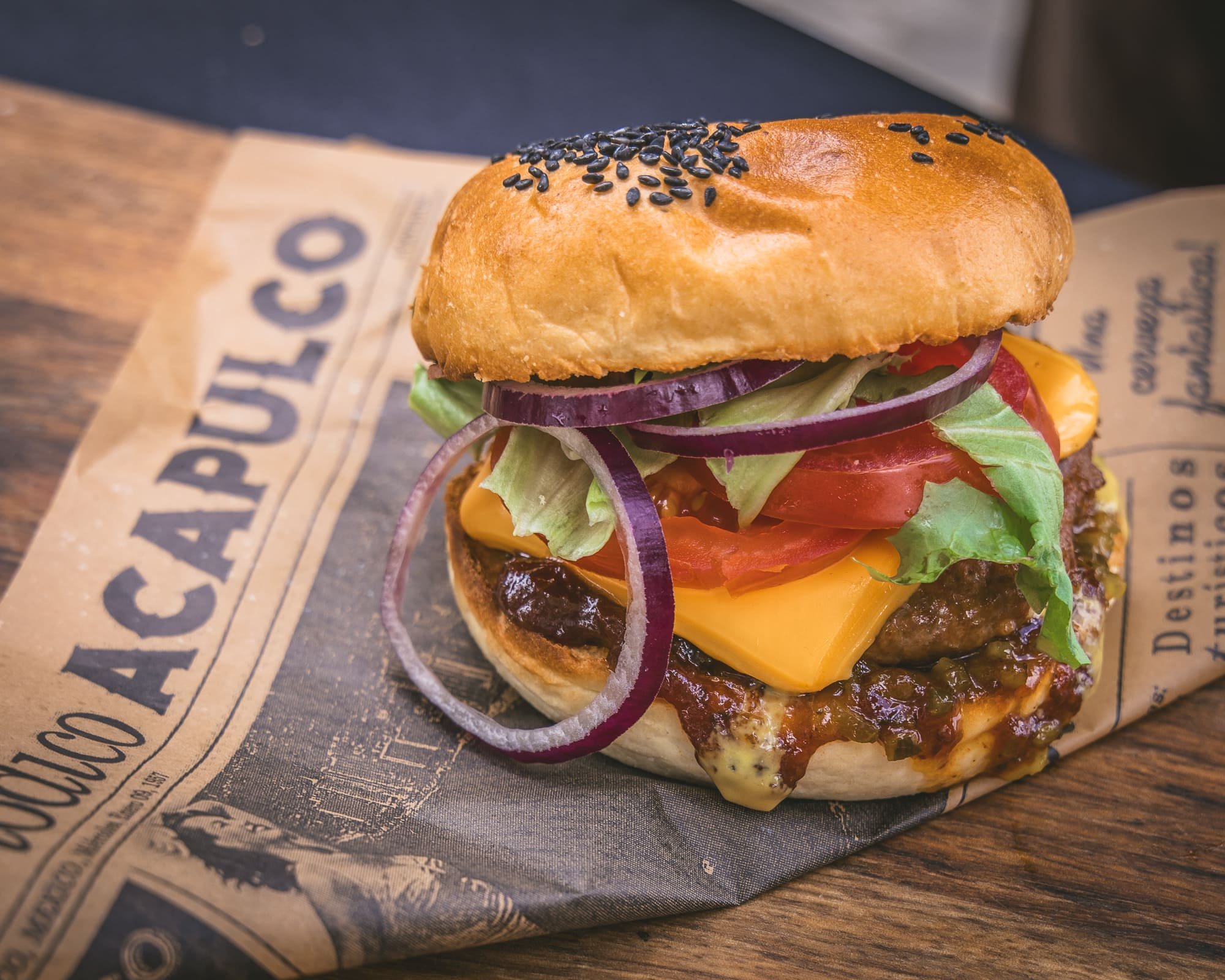 Close-up van een rundshamburger met cheddar kaas, tomaten, rode uien, sla en Irish Staut saus, op een stukje bakpapier op een houten tafel.