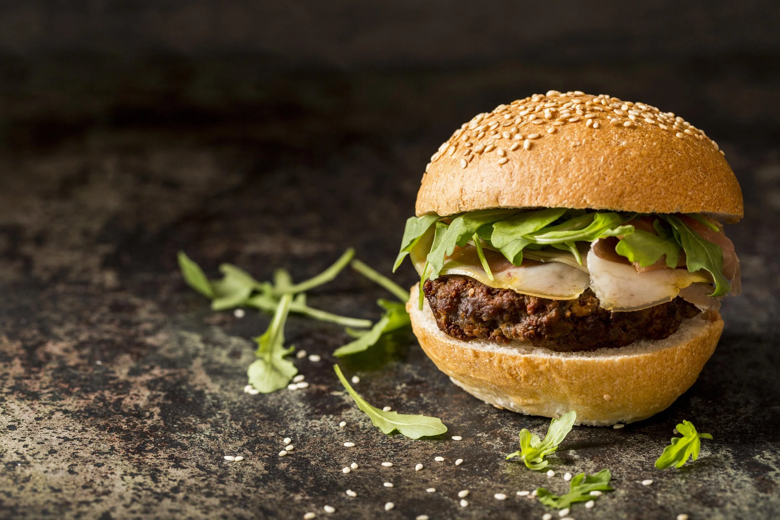 Broodje hamburger met gekruid rundvlees, Italiaanse panchetta, sla, en kaas op een donkere achtergrond.