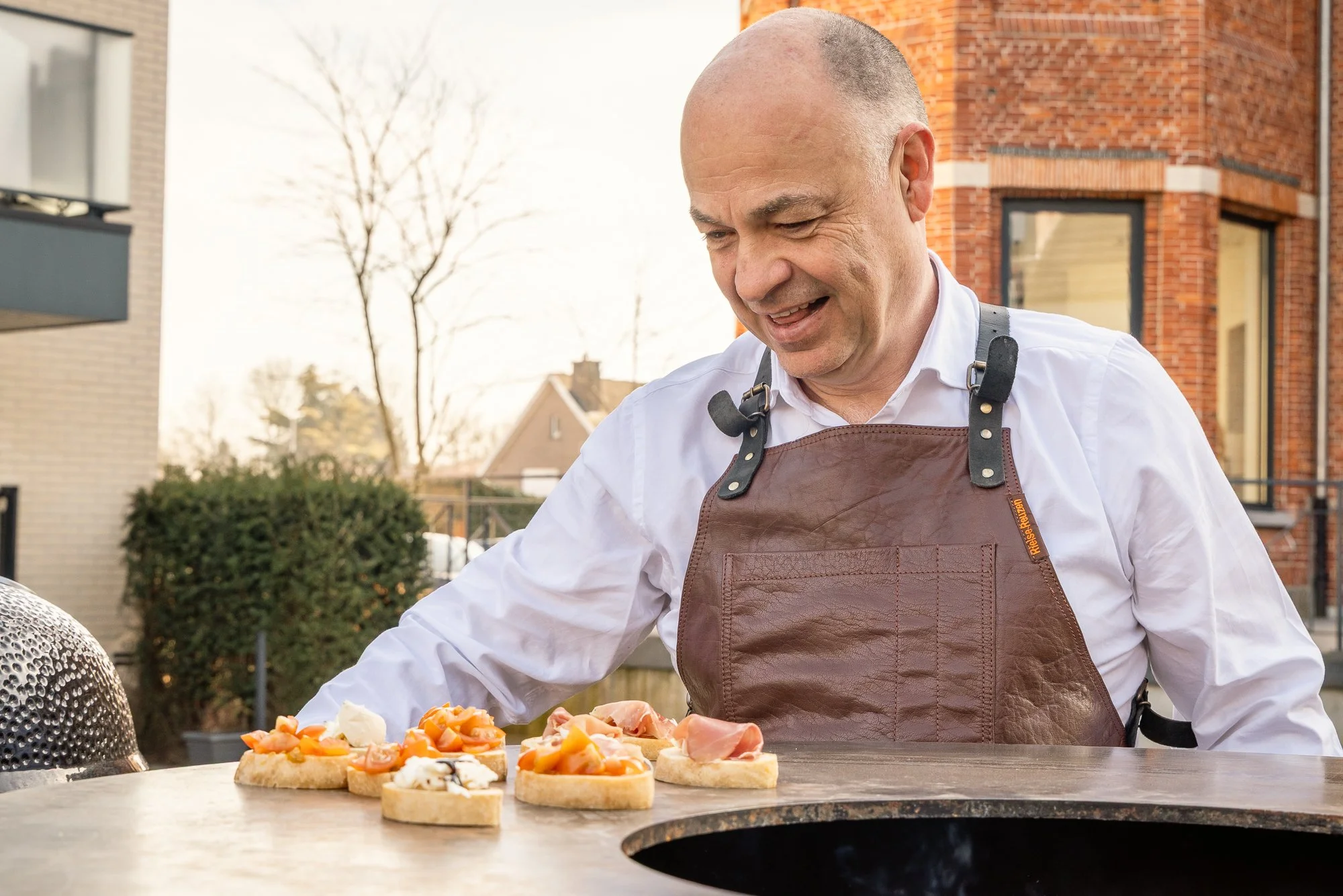 Man met een glimlach bereidt Italiaanse bruscetta's op een barbecue in openlucht.