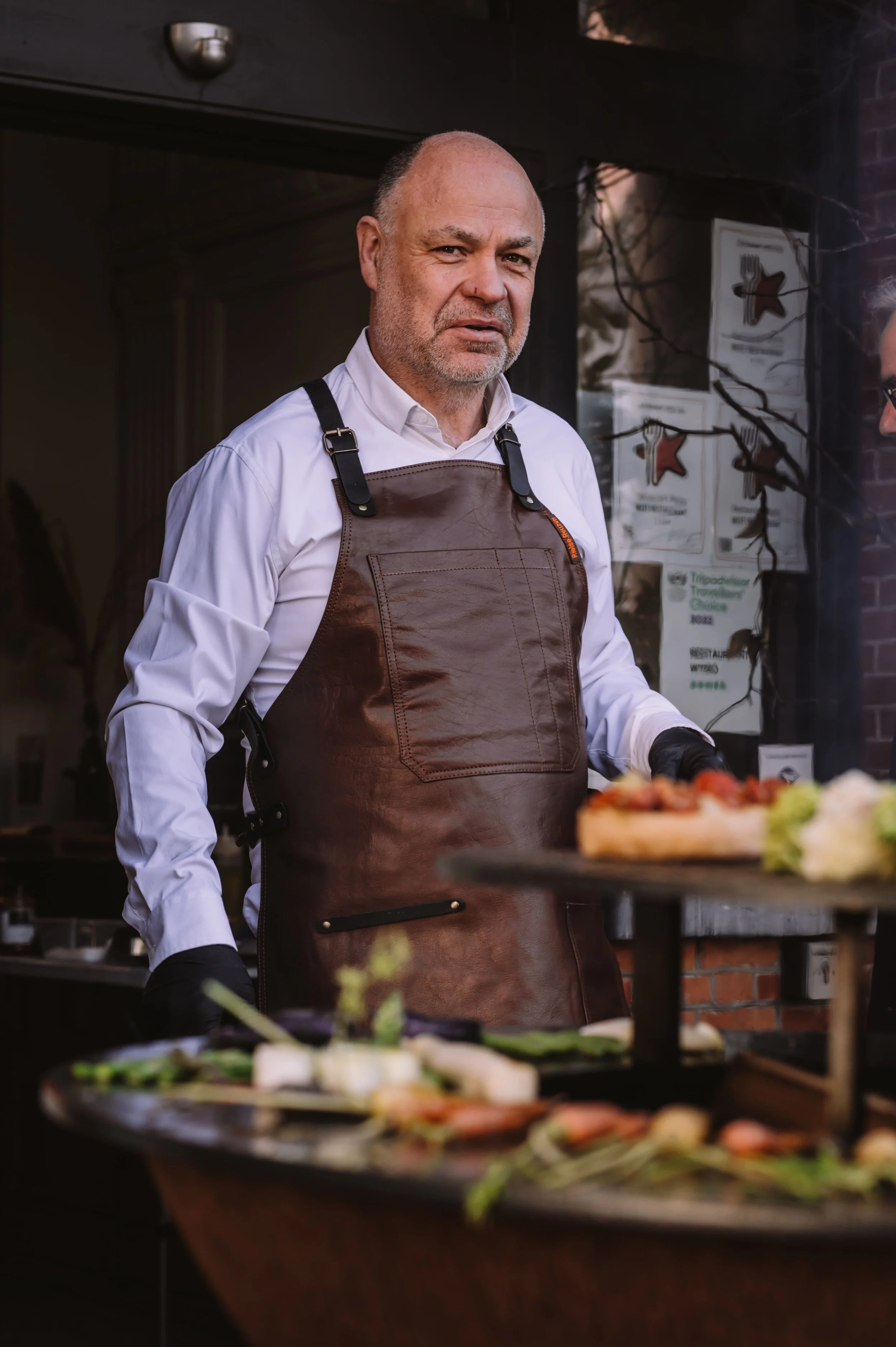 Man in witte overhemd en bruin leren schort serveert voedsel in een restaurant.