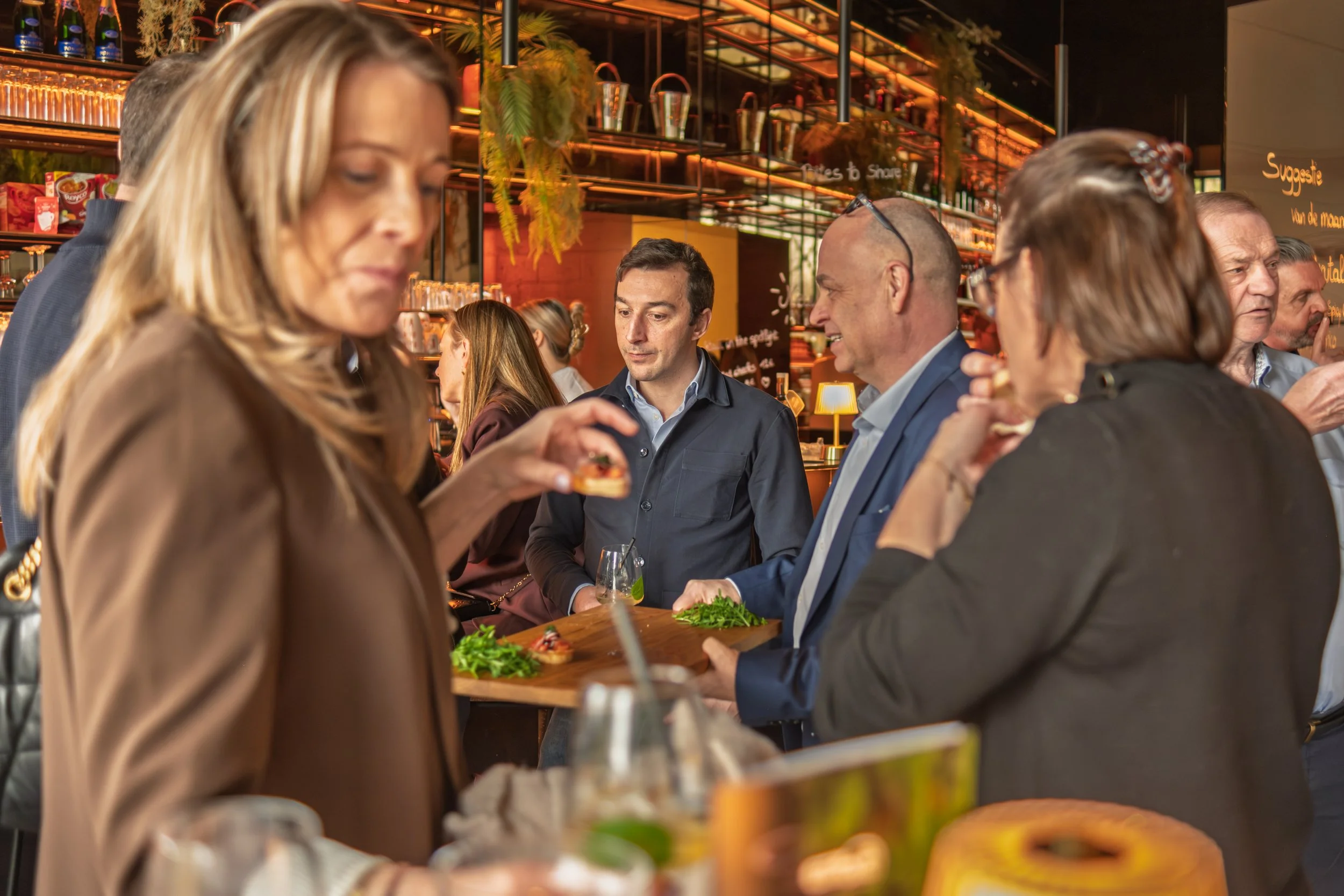 Een groep mensen dineert en drinkt in een bar met warme, sfeervolle verlichting.