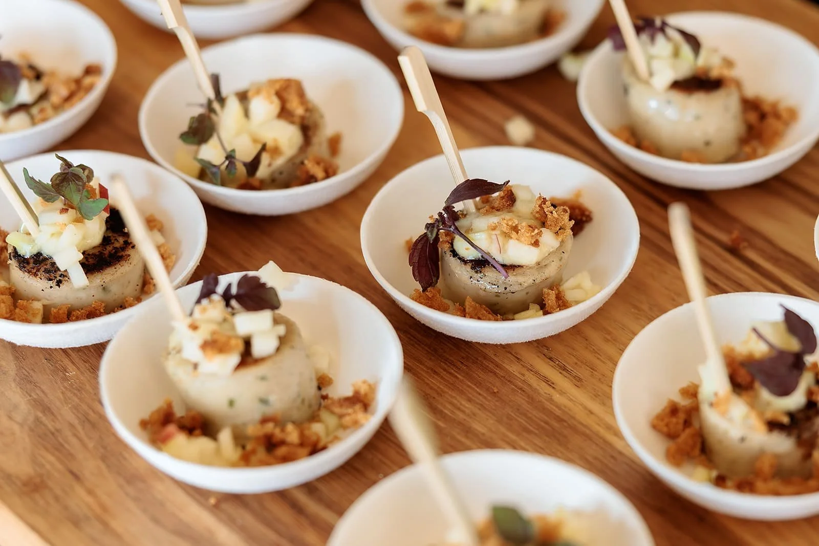 Mini, gebakken witte pens met stukjes appel en peperkoek, opgediend in kleine witte schaaltjes op een houten plank.