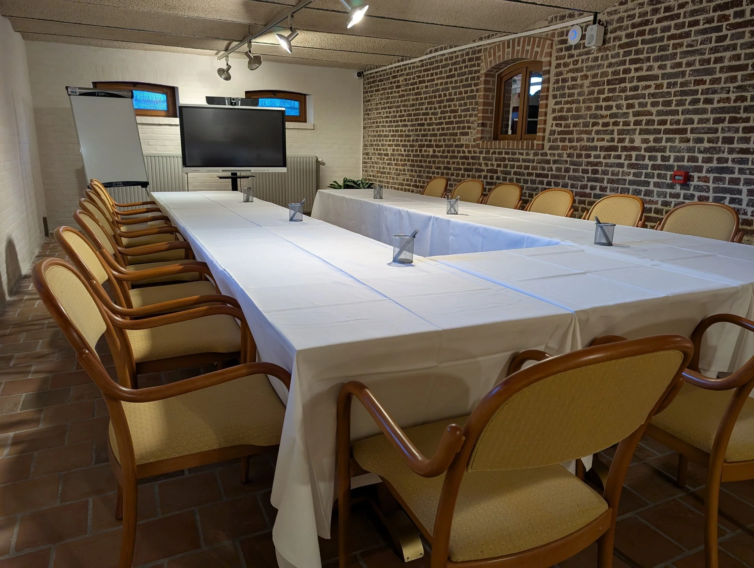 Een vergadertafel met witte tafelkleden en gele stoelen in een kamer met bakstenen muren en een scherm in het midden.