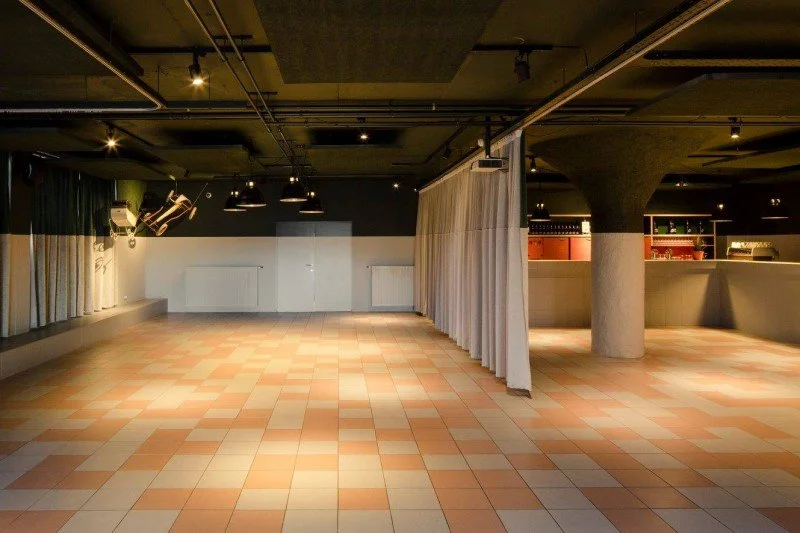 Lege dansruimte met tegelvloer, gordijnen en een centraal steunpilaar.