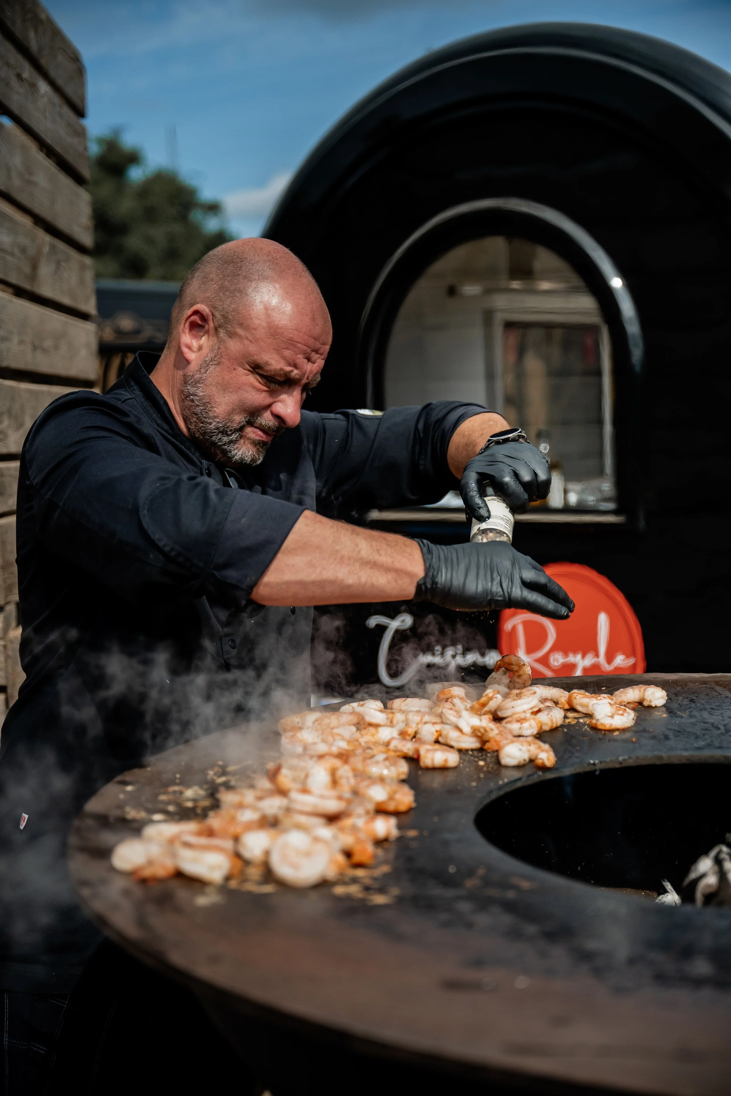 Kok achter een grote grill met garnalen, kookt of bereidt garnalen op een barbecue, buiten onder een open hemel.