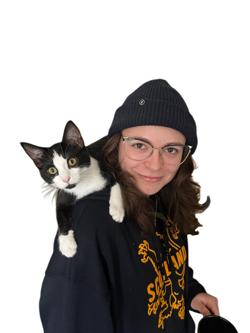young woman with glasses and a beanie hat smiling, carrying a black and white cat on her shoulder