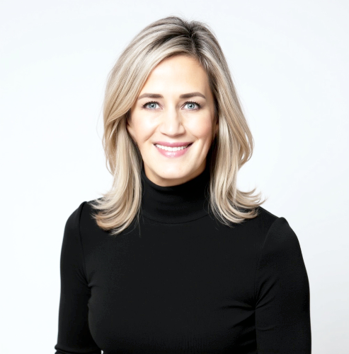 A woman with blonde hair wearing a black turtleneck, smiling against a plain white background.