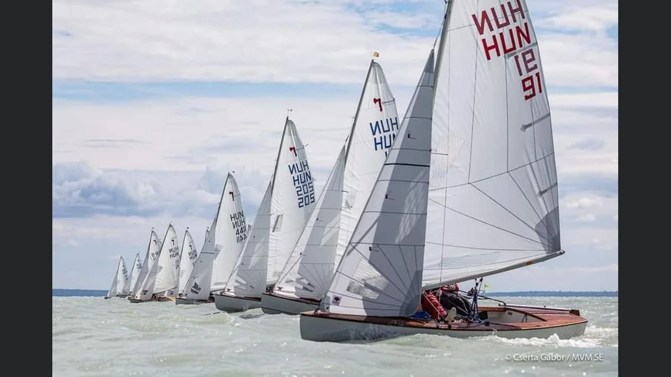 Mehrere Segelboote, die auf dem Wasser segeln, unter einem bewölkten Himmel.