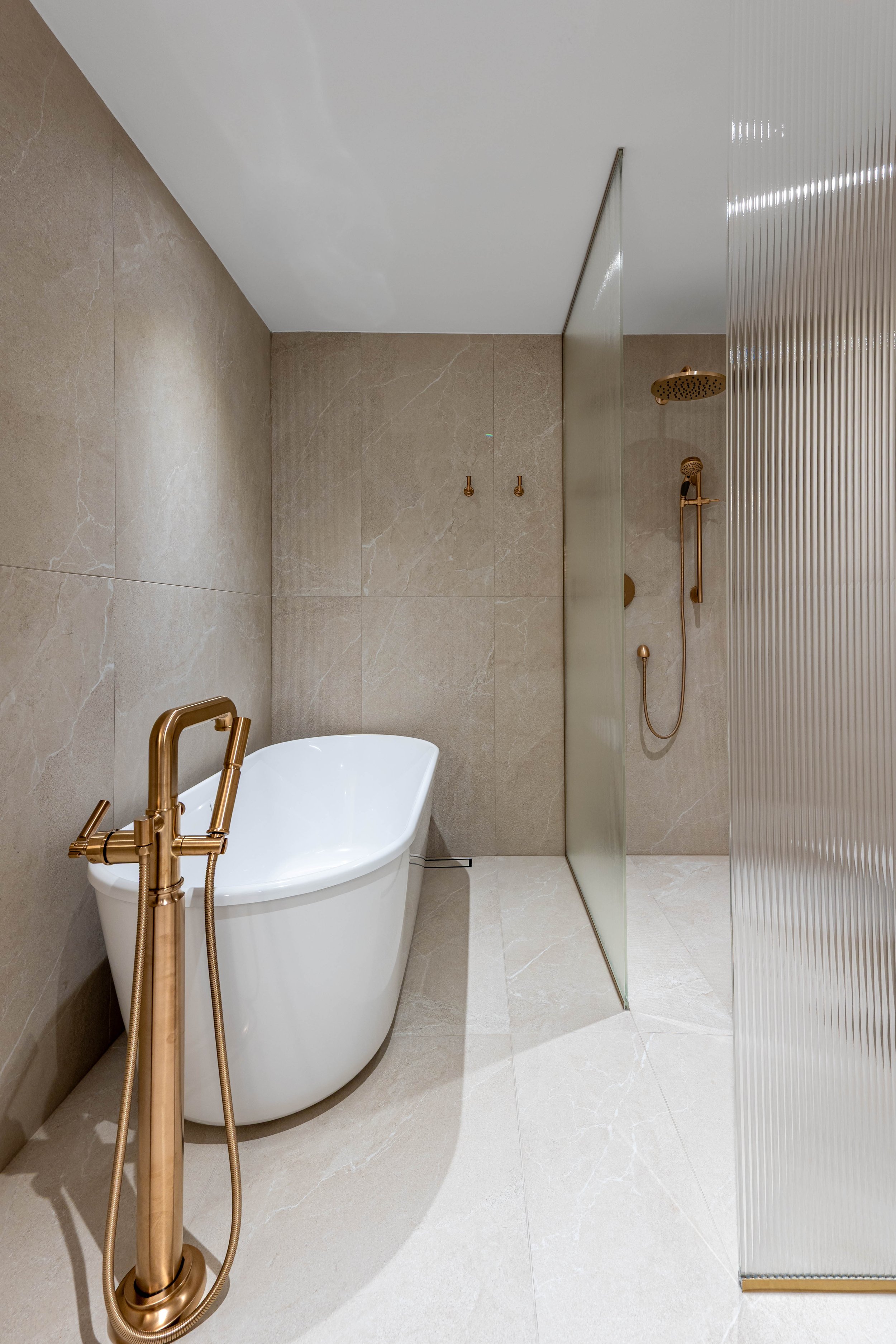 Modern bathroom with a white bathtub, gold fixtures, and a shower area separated by a gold-colored partition.