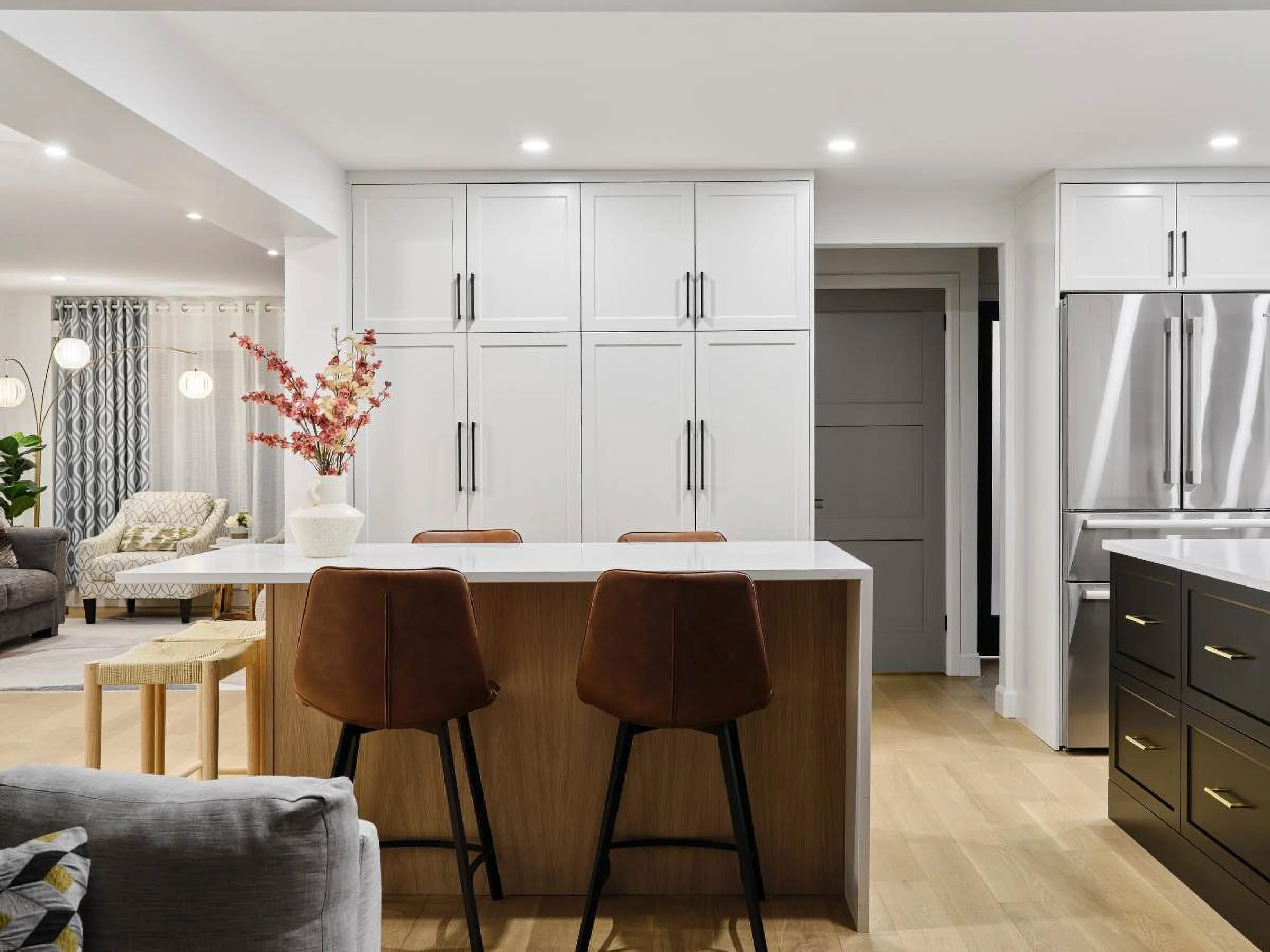 Modern kitchen with white cabinets, stainless steel refrigerator, wooden island with white countertop, brown barstools, and open living area with couches and curtains.