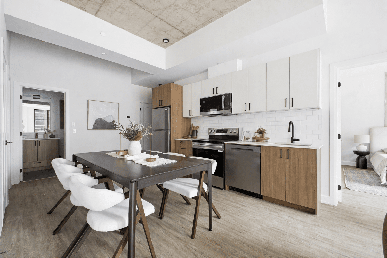 Modern kitchen with white cabinets, stainless steel refrigerator, oven, microwave, and a large kitchen island, with windows showing trees outside.