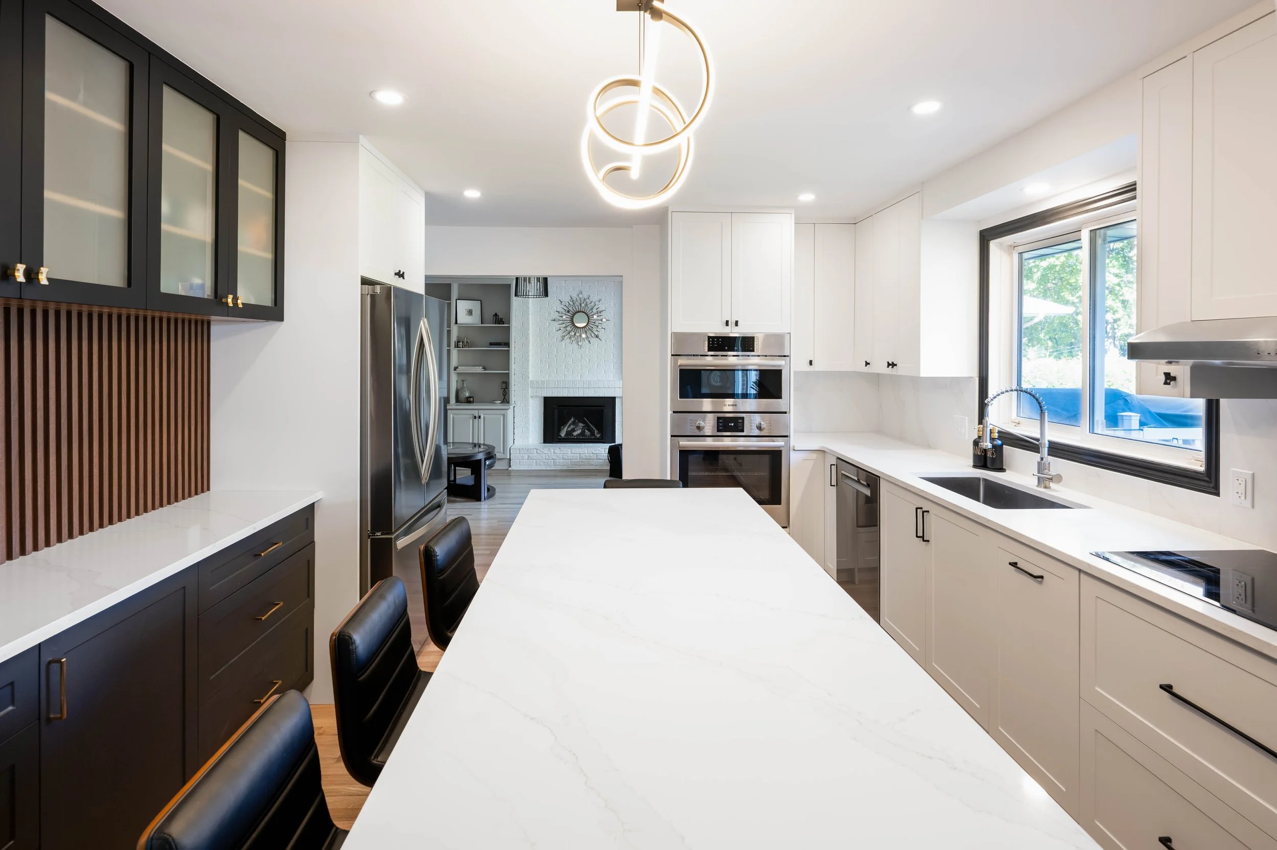 Modern kitchen with white countertops, black and white cabinets, stainless steel appliances, and a large window.
