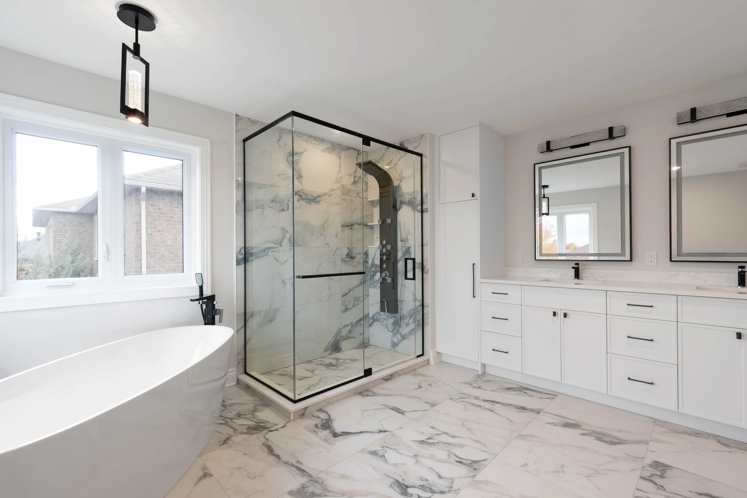 Modern bathroom with free-standing bathtub, glass shower enclosure with marble tiles, and double vanity with mirrors.