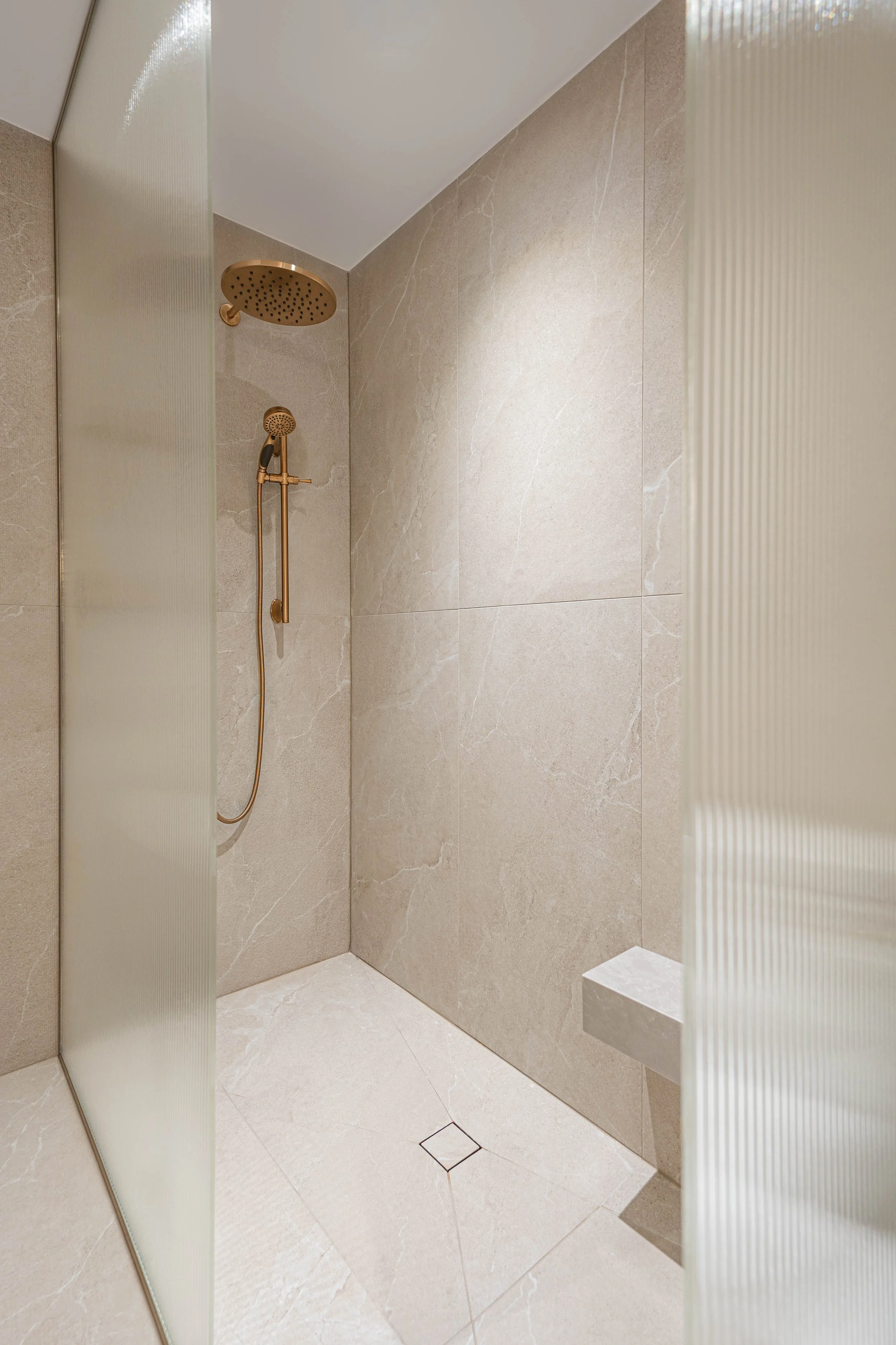 A minimalist beige shower with dual shower heads and a built-in bench.