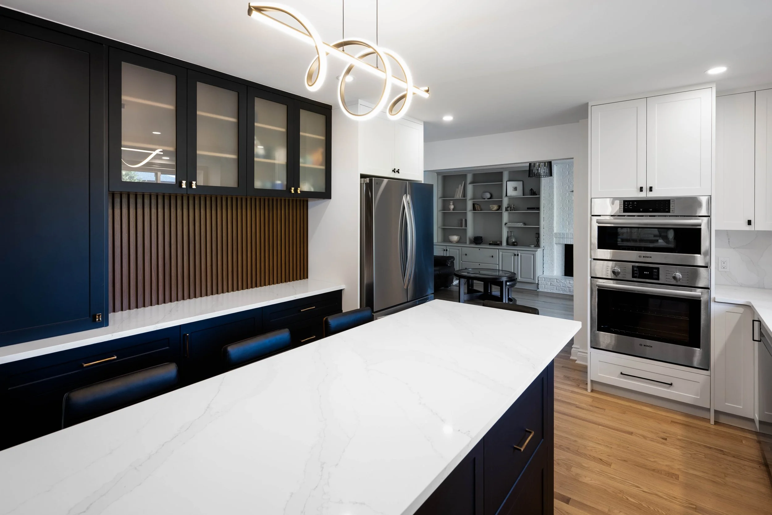 Modern kitchen with white and black cabinets, a marble island, stainless steel appliances, and a hanging light fixture.