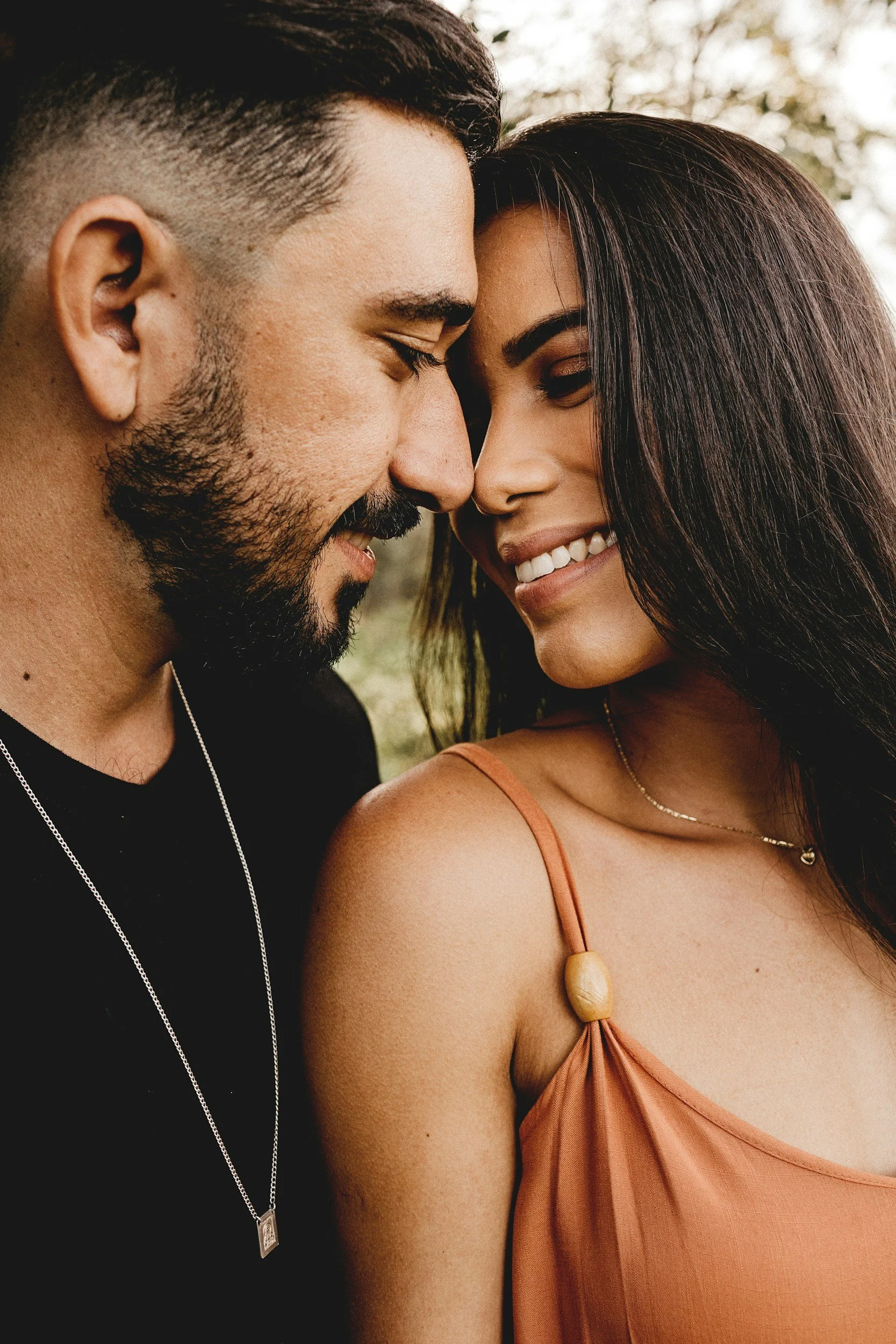 A close-up of a couple with their foreheads touching, smiling gently at each other outdoors.