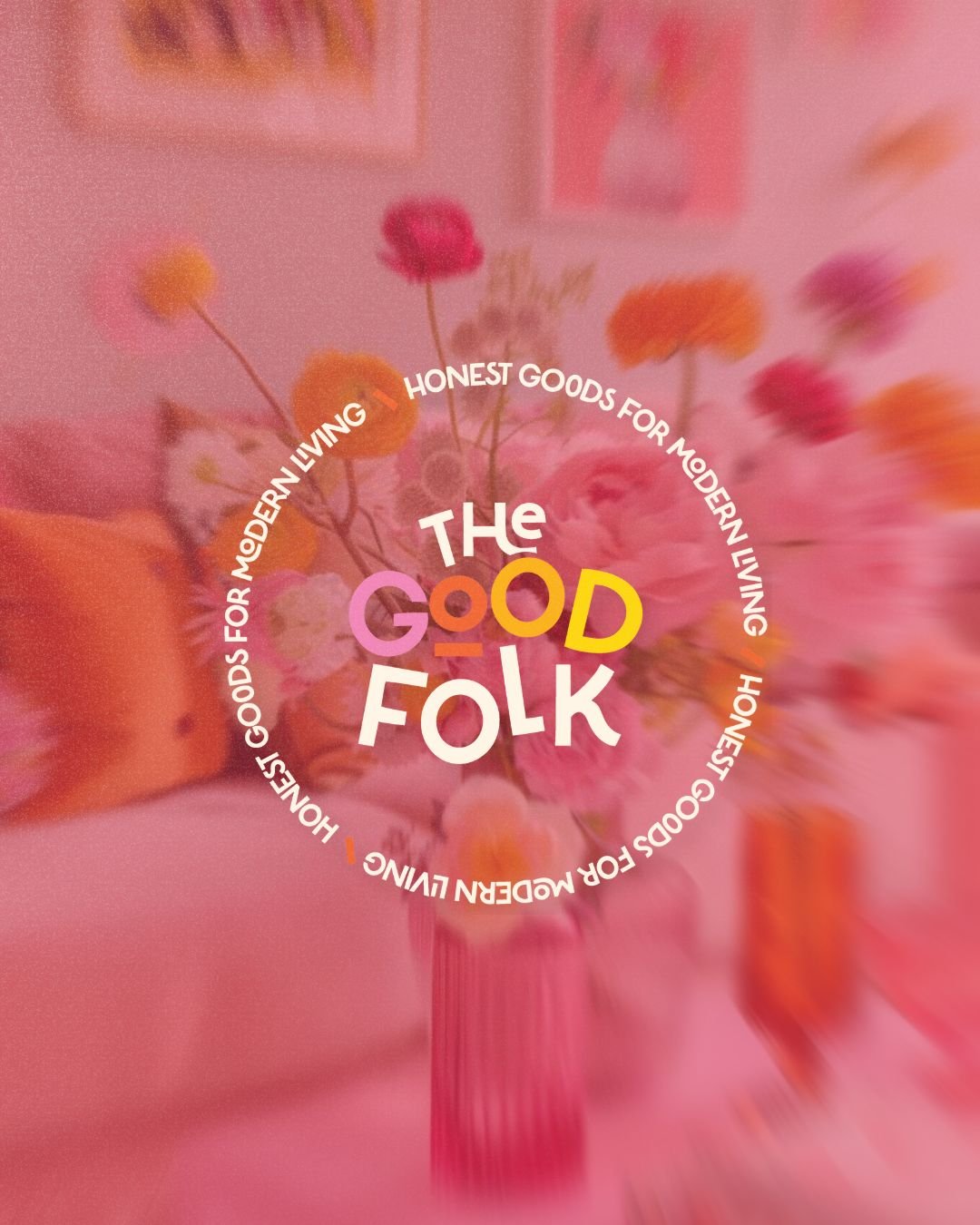 Colorful illustrated text overlaying a blurred background of flowers in a pink vase, reading 'The Good Folk' with a surrounding circular text about honest goods and modern living.