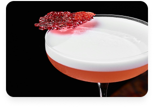 A cocktail glass with a pink and white layered drink, garnished with a red decorative sugar or candy piece on the rim.