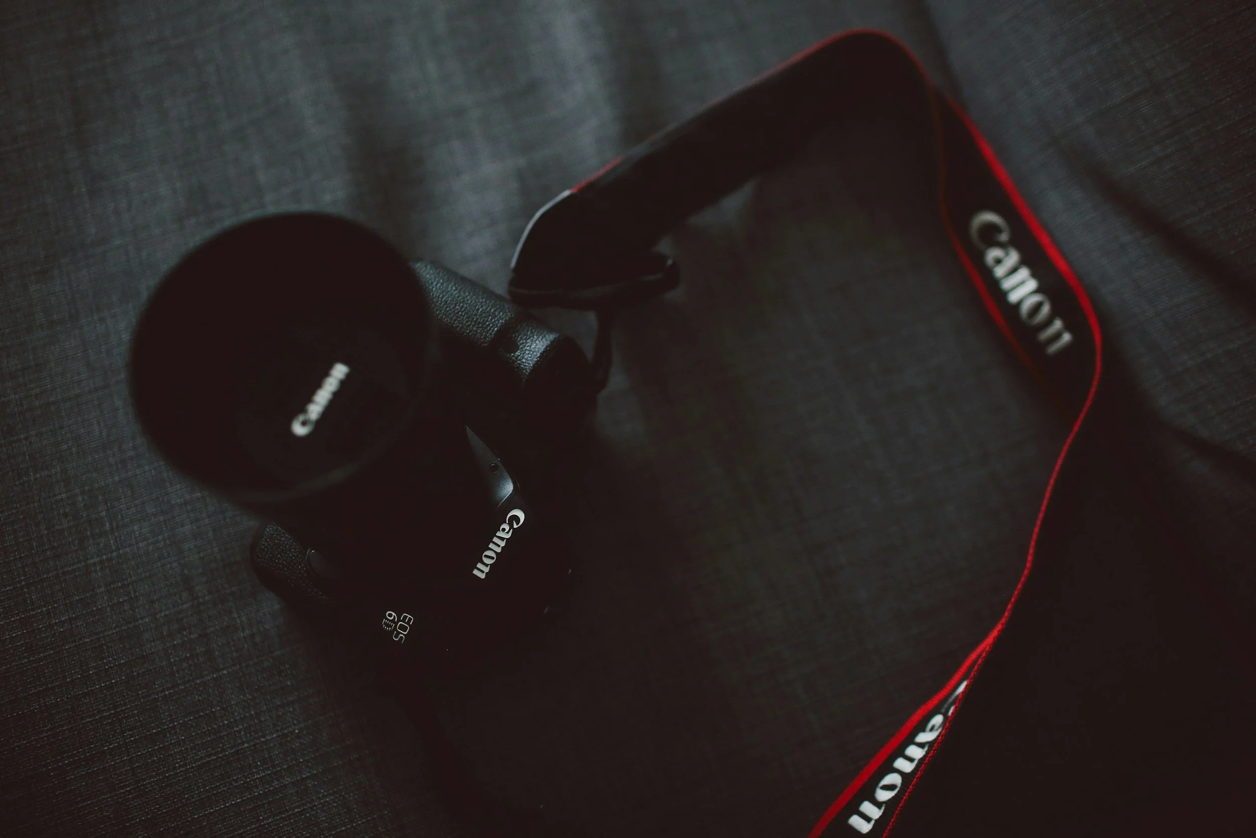 A moody image of a Canon camera laying on gray fabric.