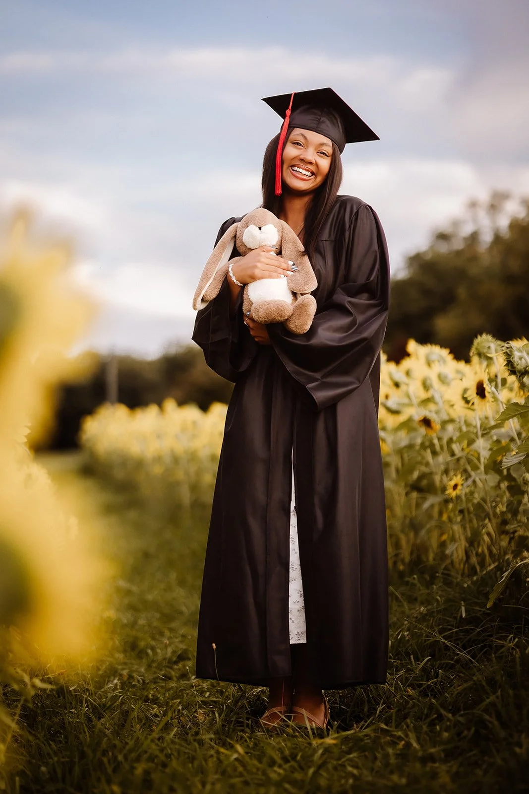Senior portrait in sunflower field with cap and gown. 