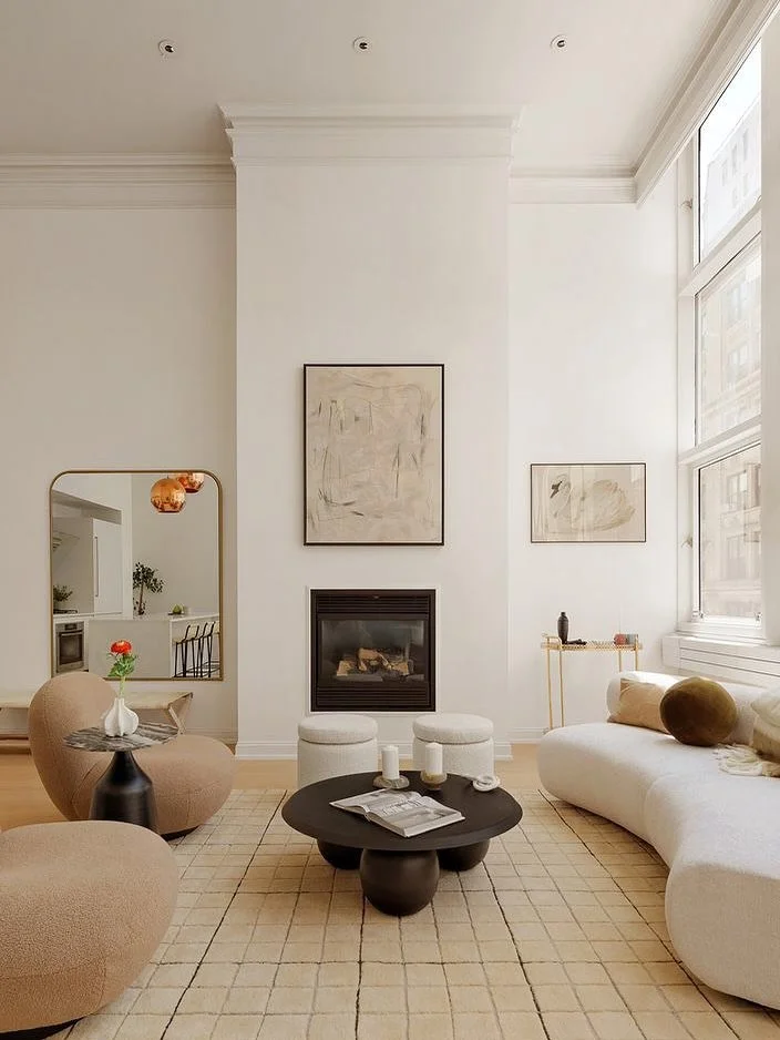 Modern living room with white walls, large window, fireplace, abstract art, beige sofa, rounded armchairs, black coffee table, and a cream rug.