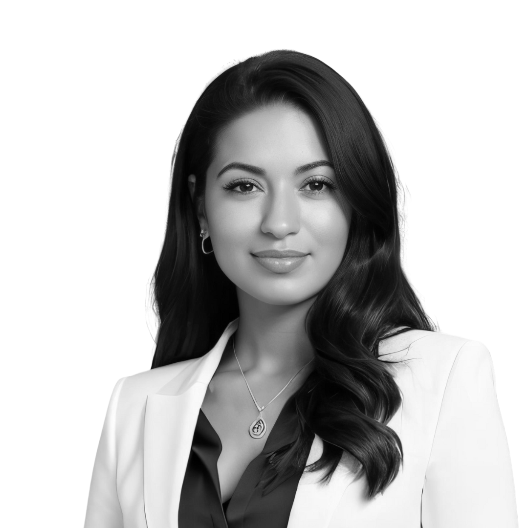 Black and white portrait of a woman with long wavy hair, wearing a white blazer, a dark top, and jewelry, smiling slightly.